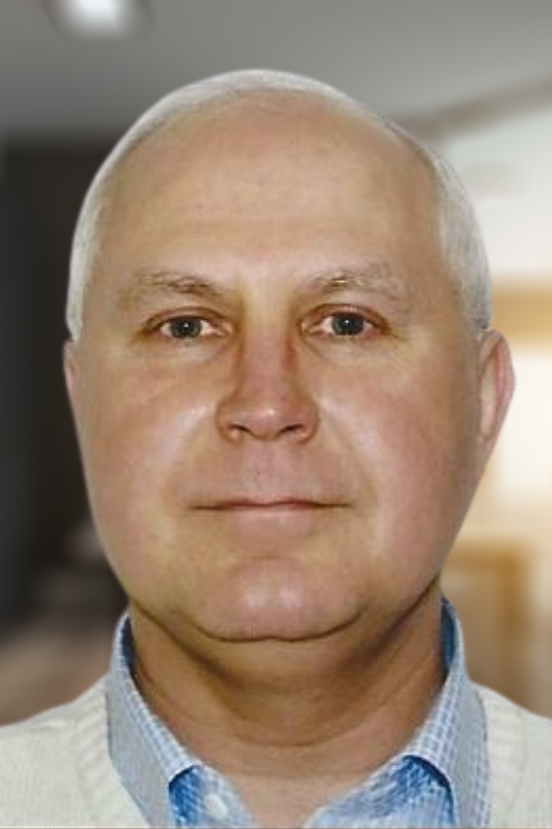 Close-up photo of a middle-aged man with a bald head, light skin, blue eyes, and wearing a light-colored collared shirt, in an indoor setting.