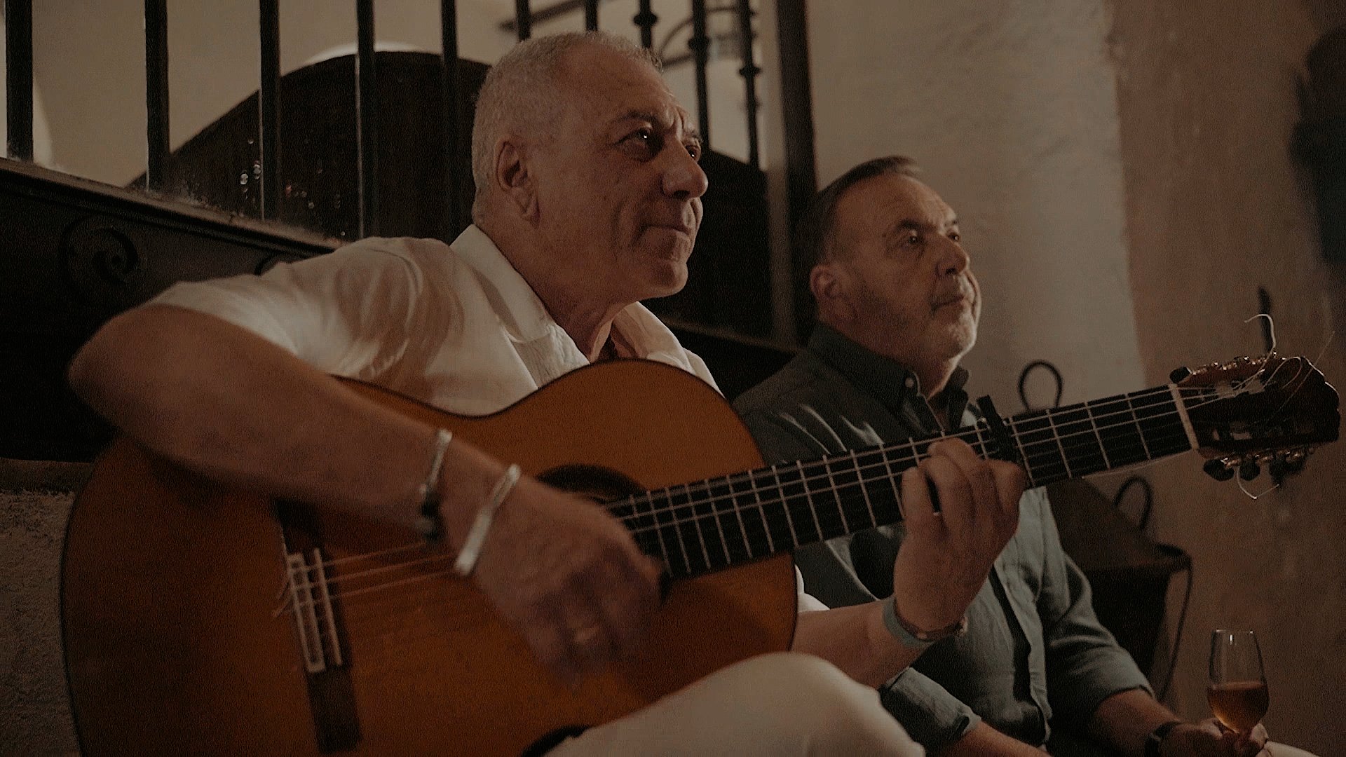 Dos hombres tocando la guitarra y cantando en un lugar con poca luz.
