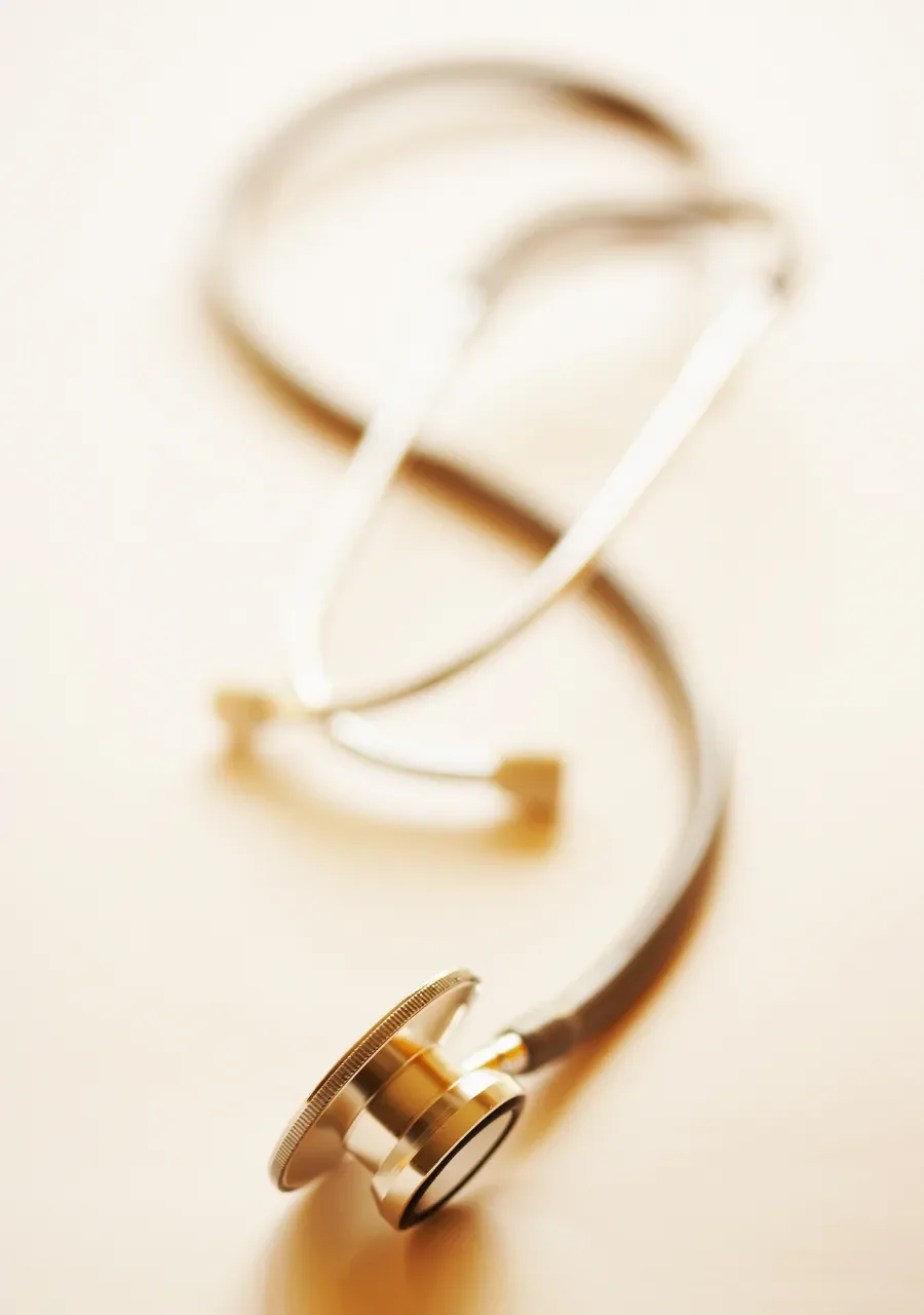 A close-up of a stethoscope with a gold-colored chest piece and white tubing on a cream background.