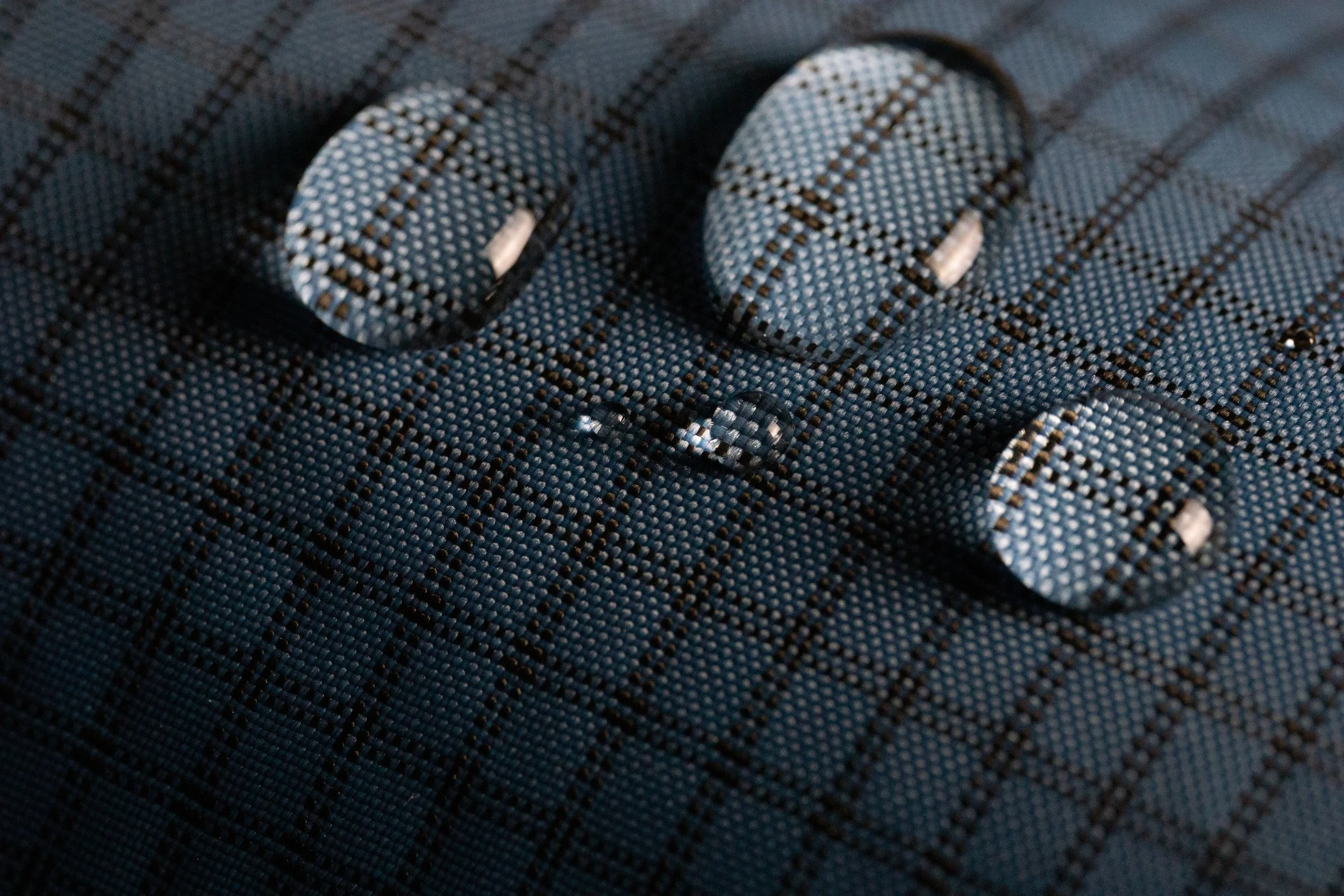 Zoom sur un tissu noir en maille avec quatre boutons en plastique noir, deux visibles en haut et deux en bas, tous cousus sur le tissu avec des points noirs.
