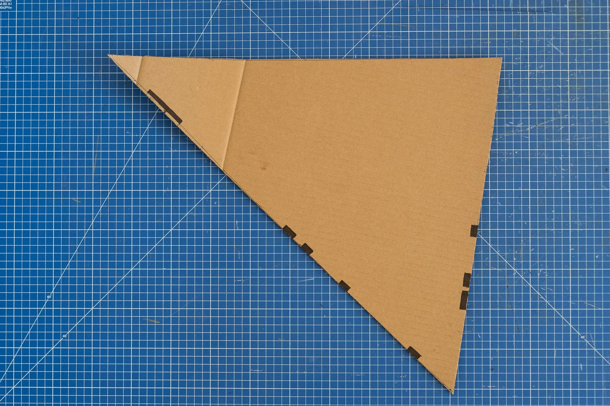 Une pièce de carton pliée en triangle sur une surface de découpe bleue avec des quadrillages.