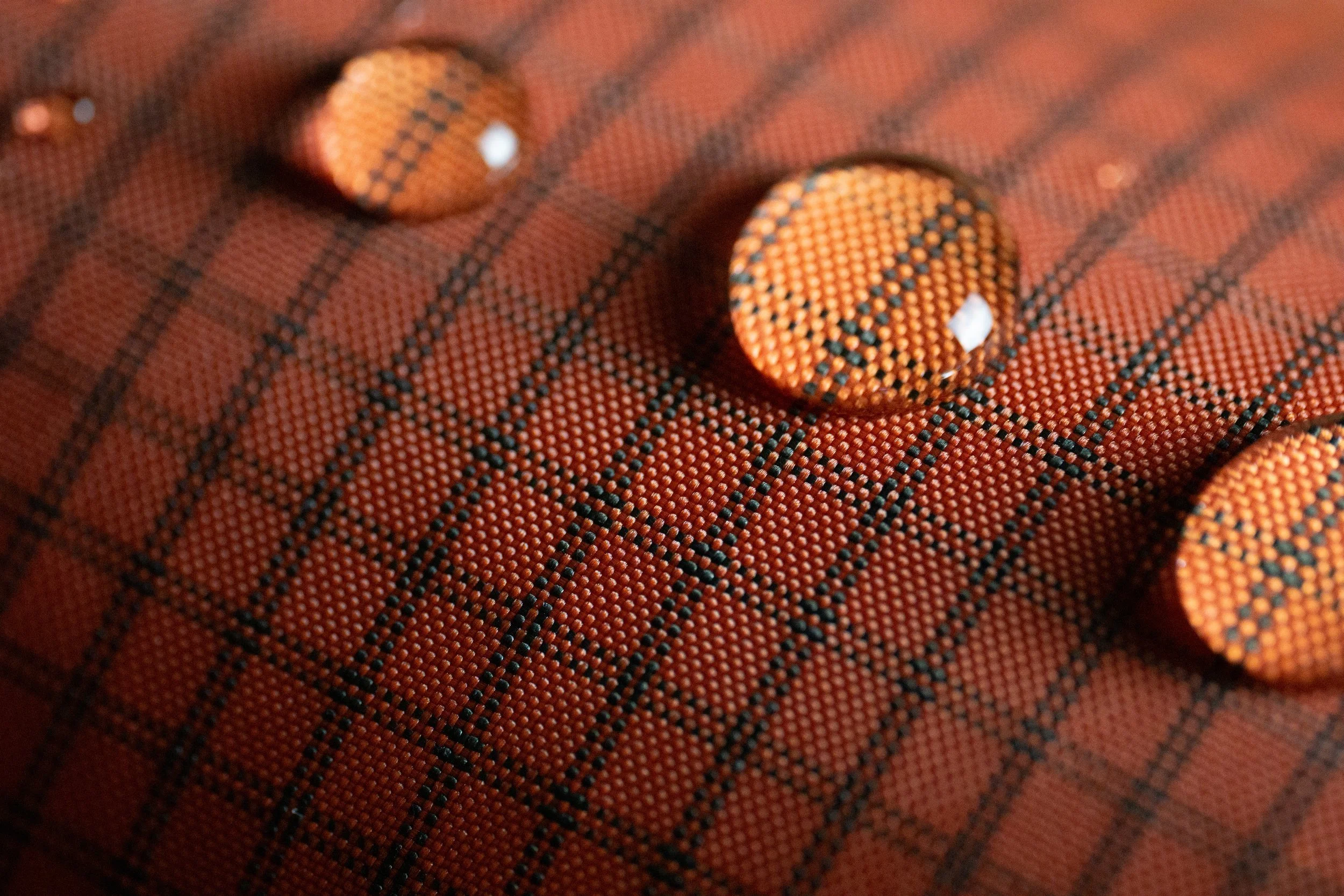 Gouttes d'eau sur un tissu en coton à motif tartan orange et noir.