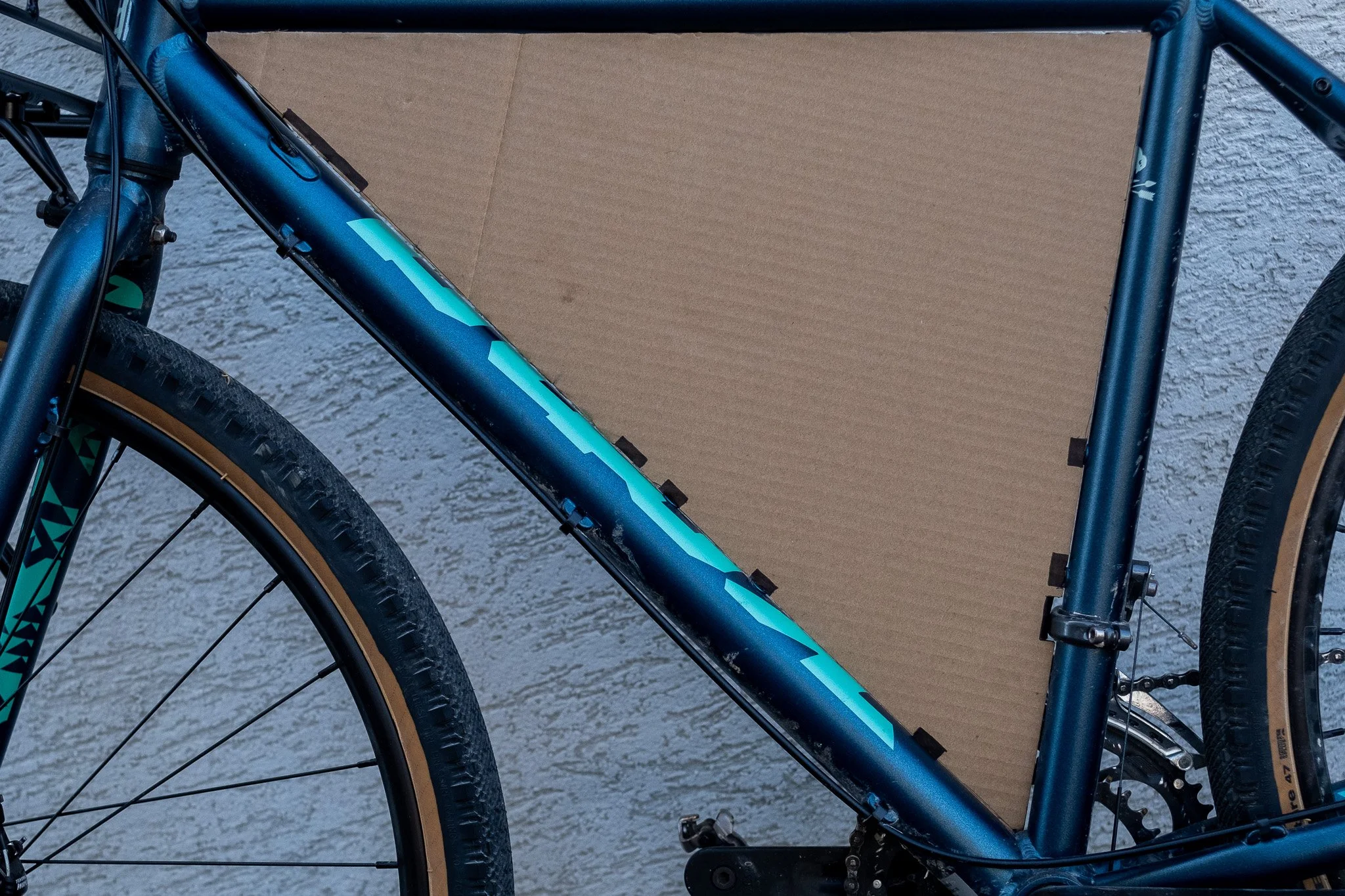 Photo d'un vélo de montagne bleu avec des pneus à crampons, placé contre un mur en béton avec une planche en bois derrière.
