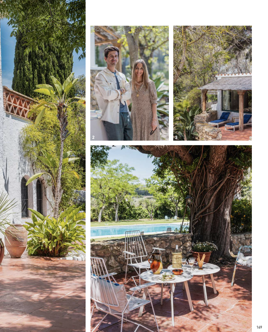 Une terrasse avec un mobilier en métal blanc, un grand arbre et une piscine en arrière-plan, entourée de verdure et de nature