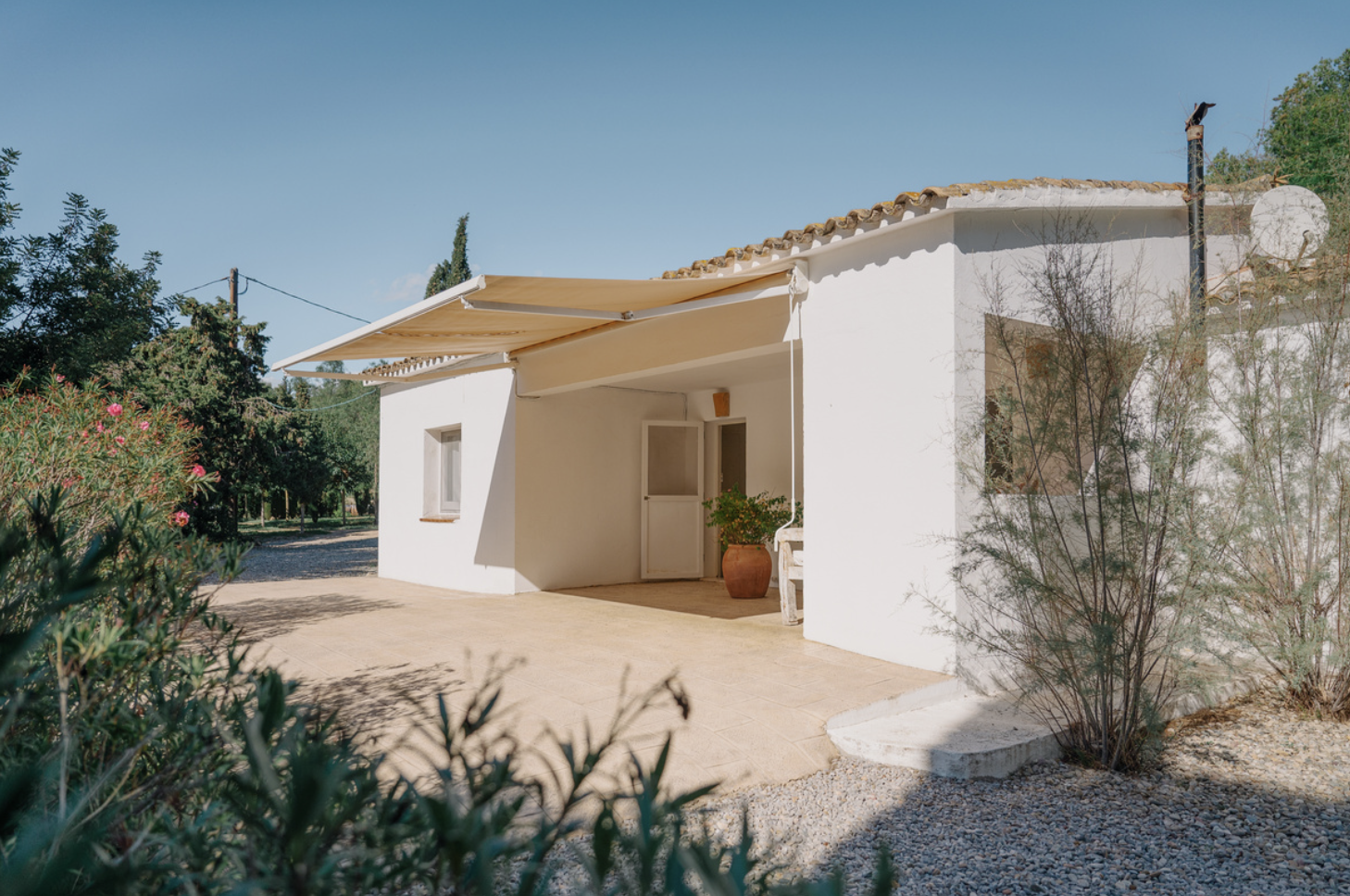 Maisons blanches avec une terrasse couverte, un puit et des plantes dans un environnement ensoleillé.