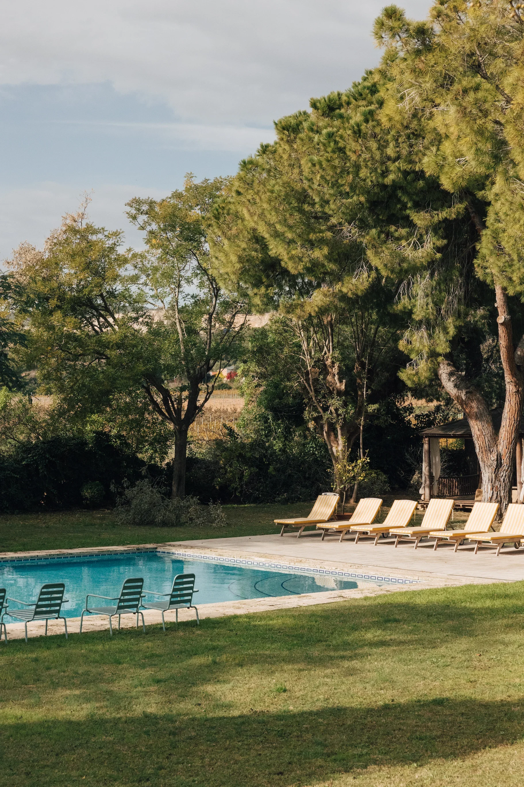 Piscine extérieure entourée de chaises longues jaunes et d'arbres verts dans un jardin paisible.