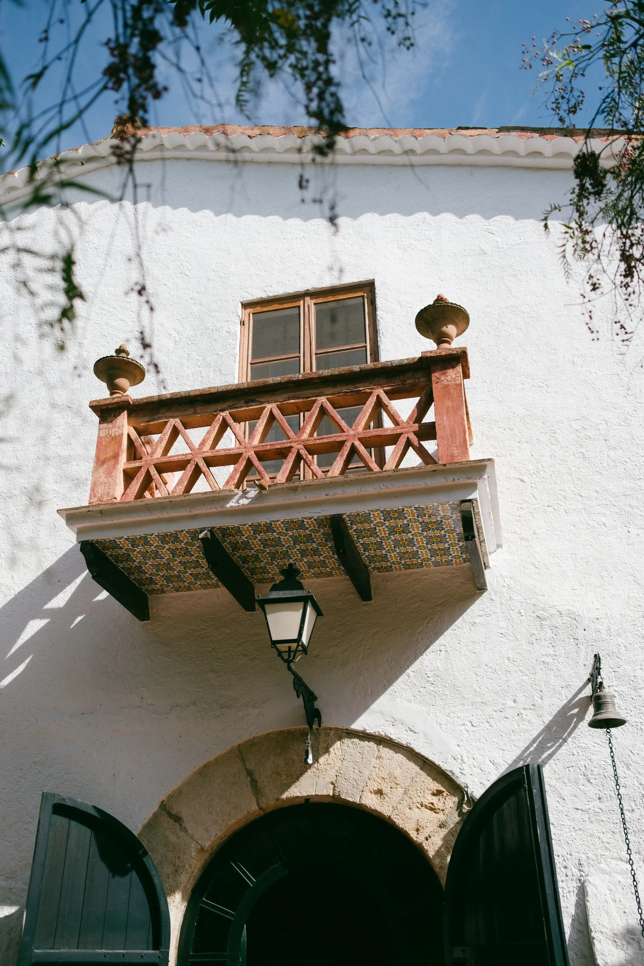 Façade d'une maison blanche avec balcon en bois, fenêtre et lanterne suspendue.