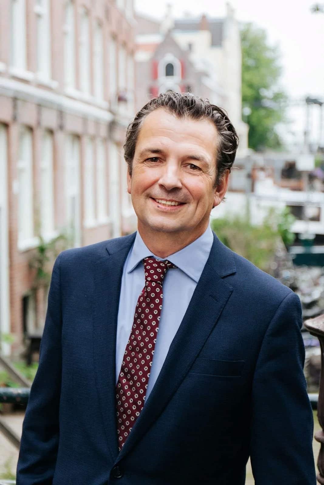 Gertjan Teeuwen in a suit and tie outdoors with buildings in the background