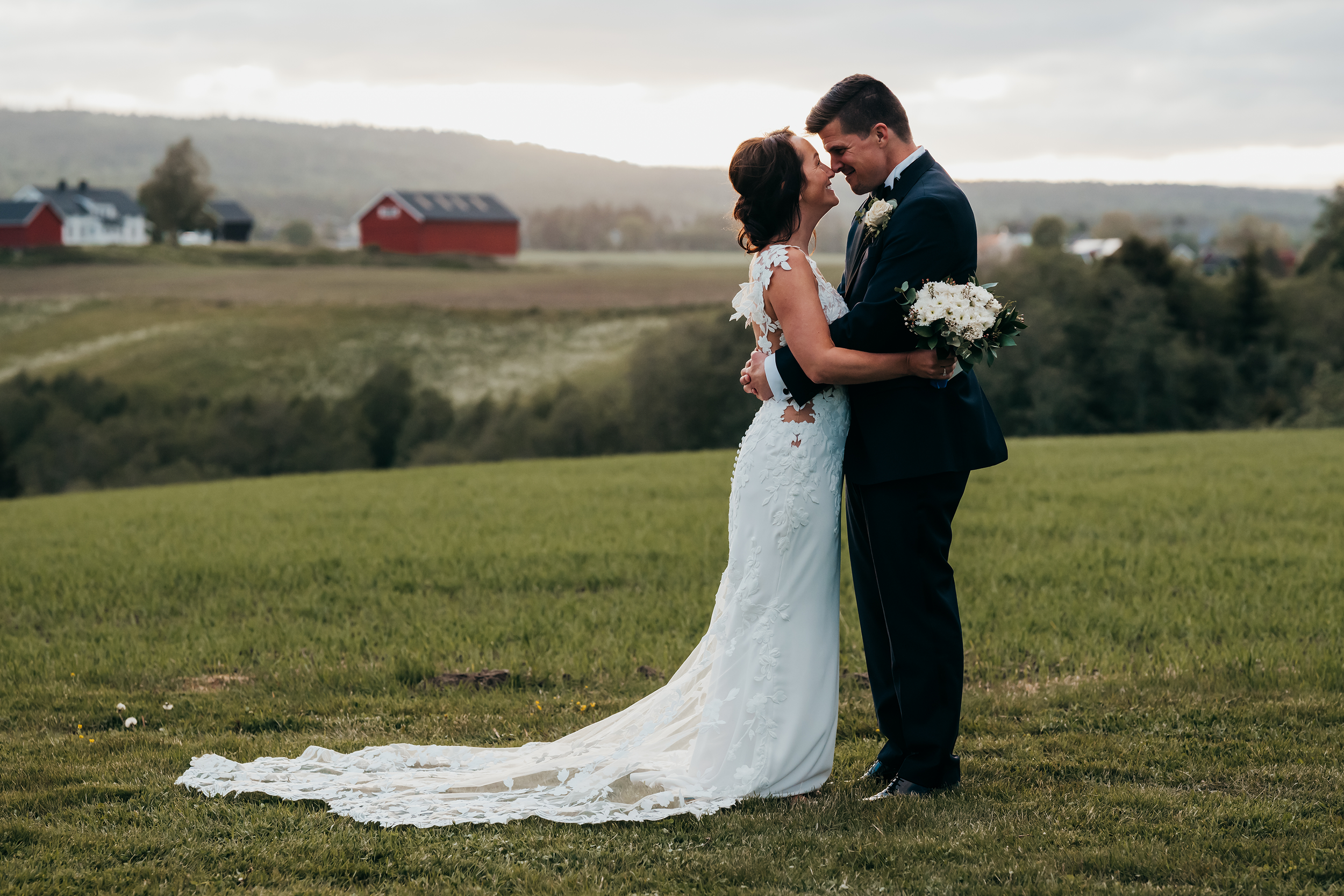 Burdepar som ser varmt på hverandre i solnedgang i et vakkert landskap på landet med en gård bak dem.