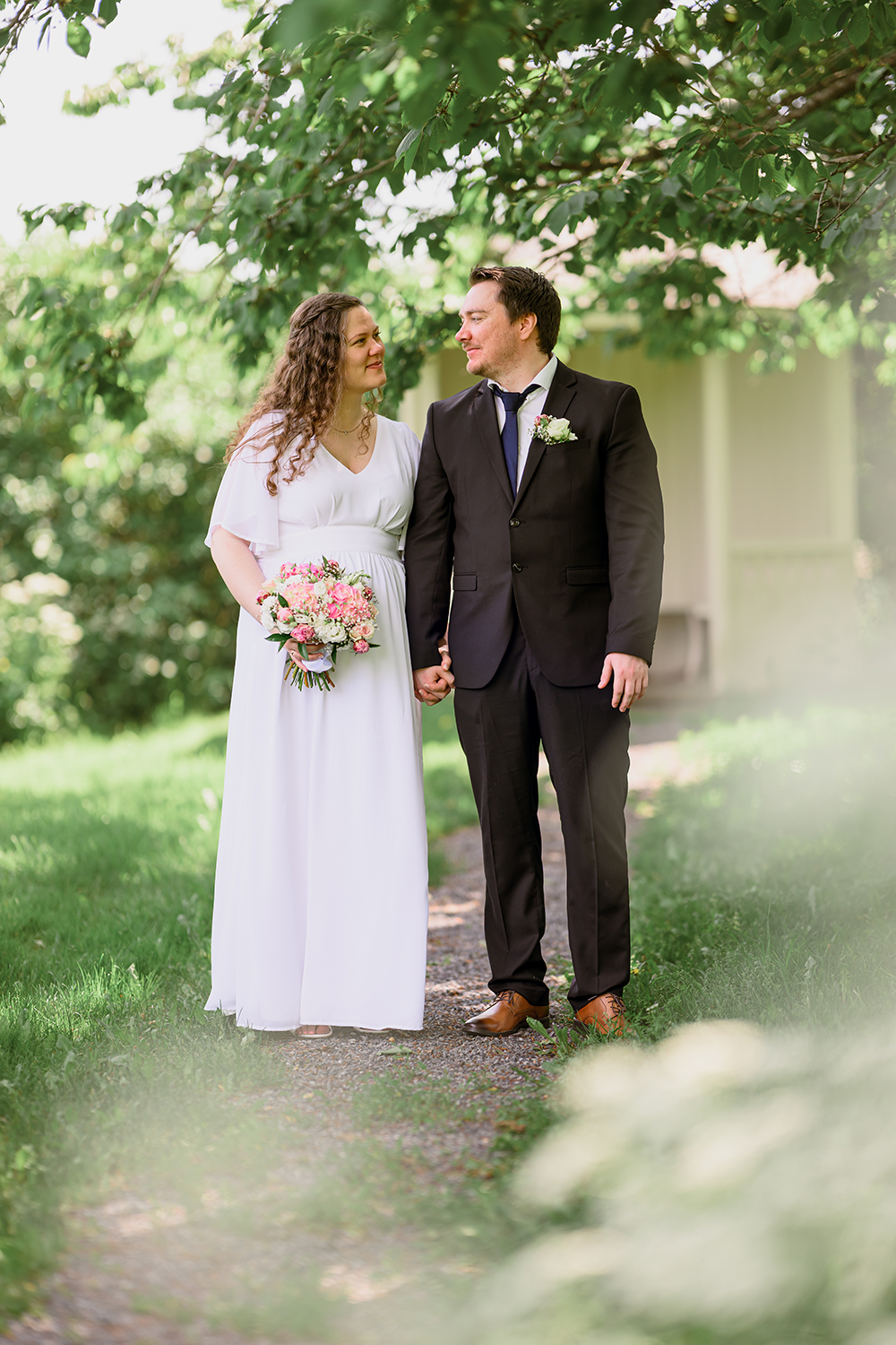 Nygift ektepar ser ømt på hverandre i en romantisk grønn hage. Kona har på seg en fin hvit kjole med en nydelig dusfarget blomsterbukett