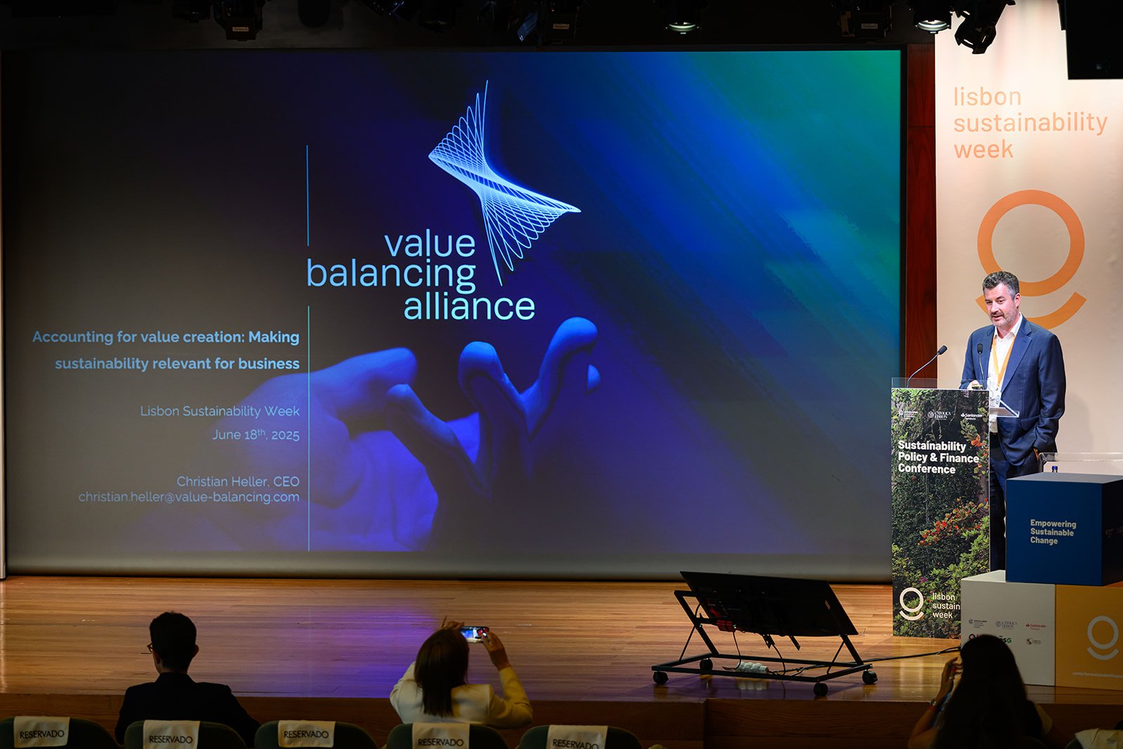 A man in a suit giving a presentation at the Lisbon Sustainability Week conference. The slide behind him reads 'value balancing alliance' and 'Accounting for value creation: Making sustainability relevant for business, Lisbon Sustainability Week, Jun