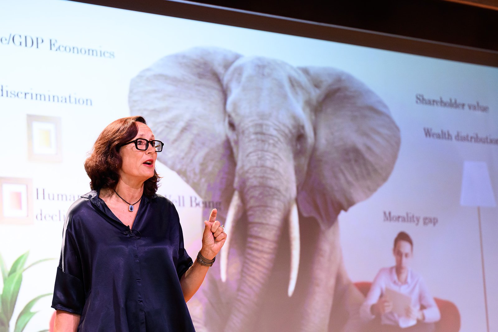Woman with dark brown hair and glasses giving a presentation in front of a slide with an elephant image and text.