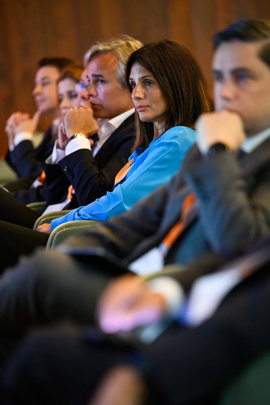 A group of businesspeople sitting in an audience at a conference, focusing on a speaker.