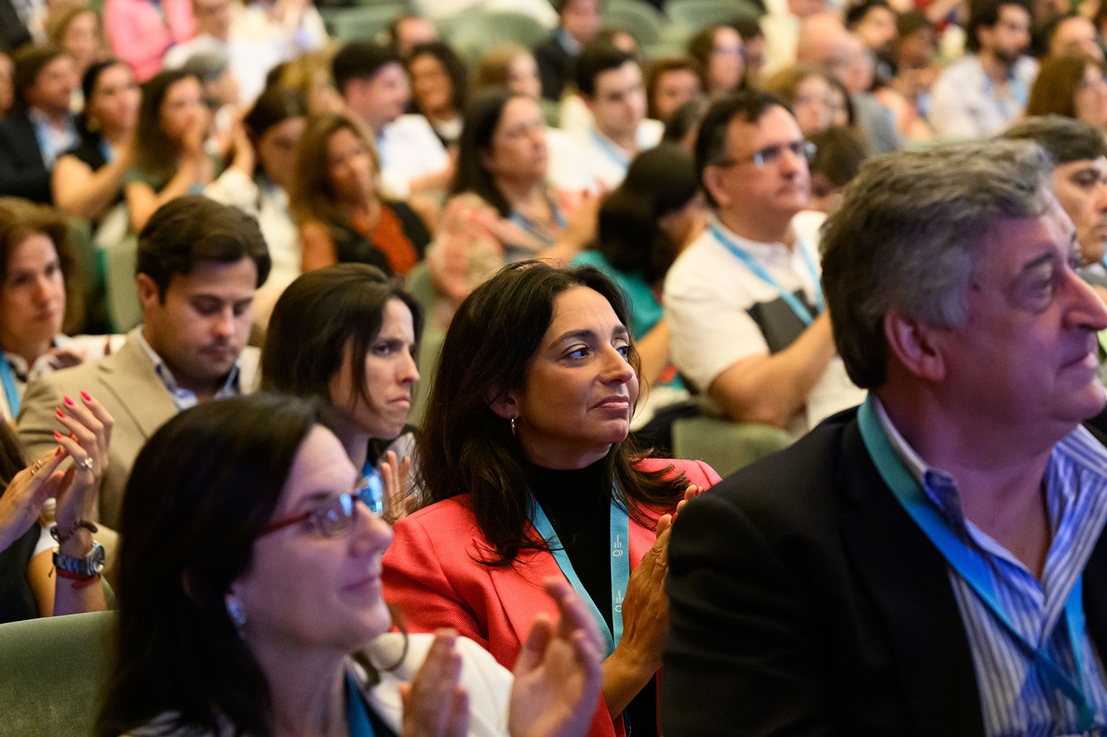 Audience members attending a conference, some clapping, in a large indoor auditorium.