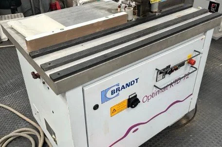 Una máquina para lijar madera con marca 'BRANDT' y una superficie de trabajo de madera sobre ella.