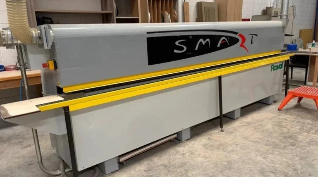 Maquina de corte de madera en taller con mesa de trabajo y estantes en el fondo.