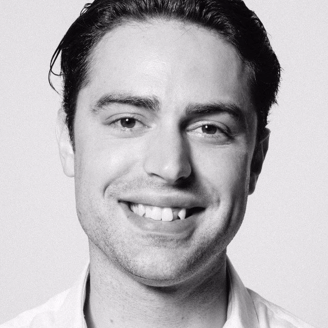 Black and white portrait of a smiling man with dark hair, wearing a collared shirt.