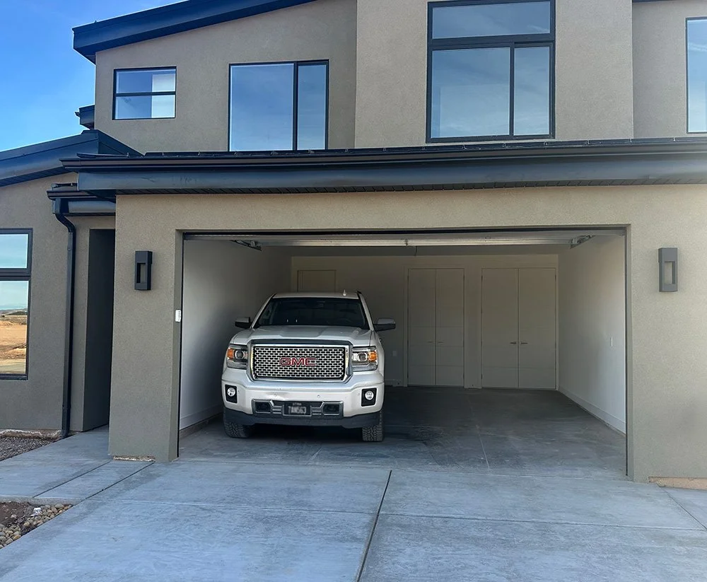 Modern white house with black accents, featuring a red car in the driveway.