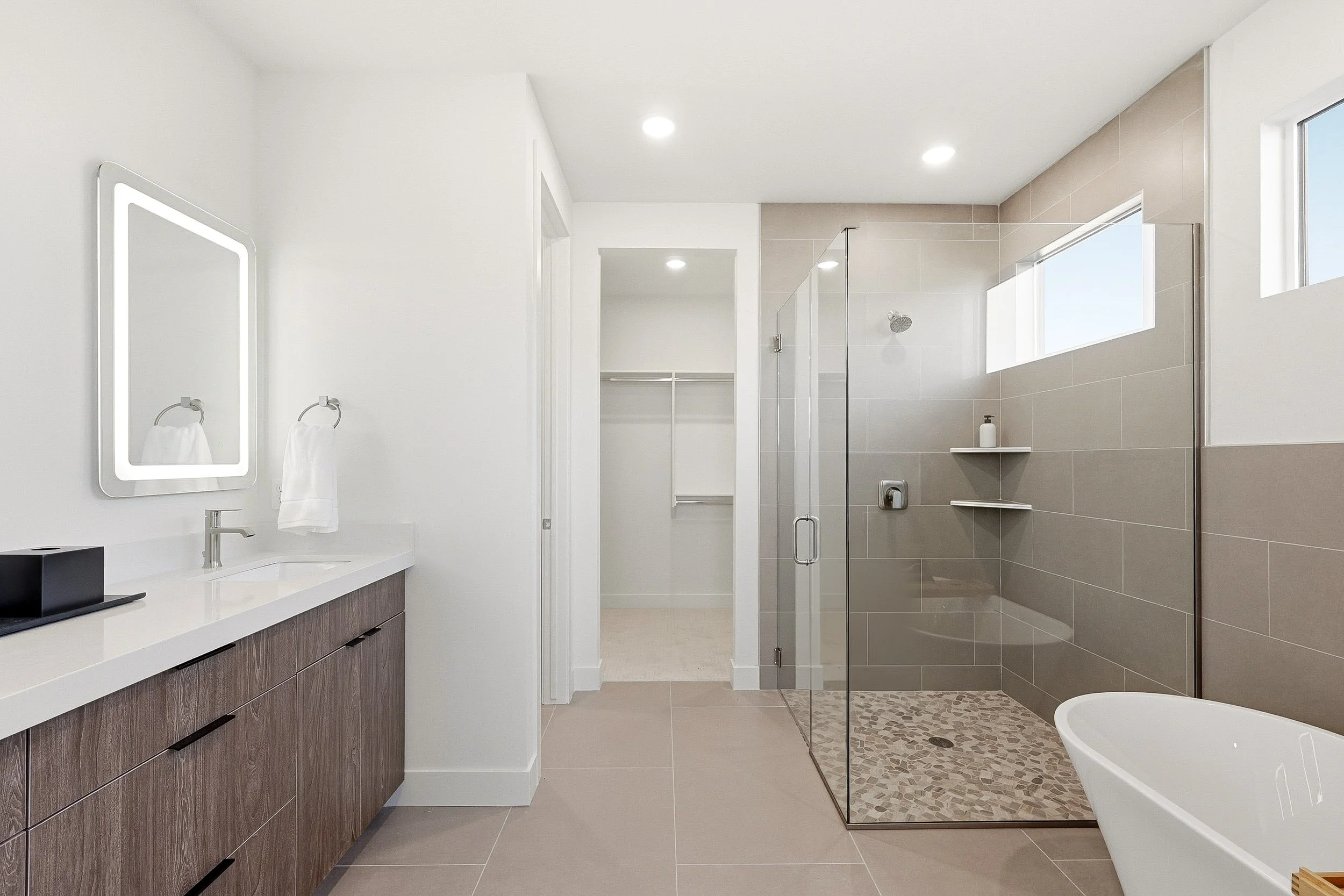 Modern bathroom with a glass-enclosed shower, a toilet, a double vanity with black fixtures, and a large mirror.