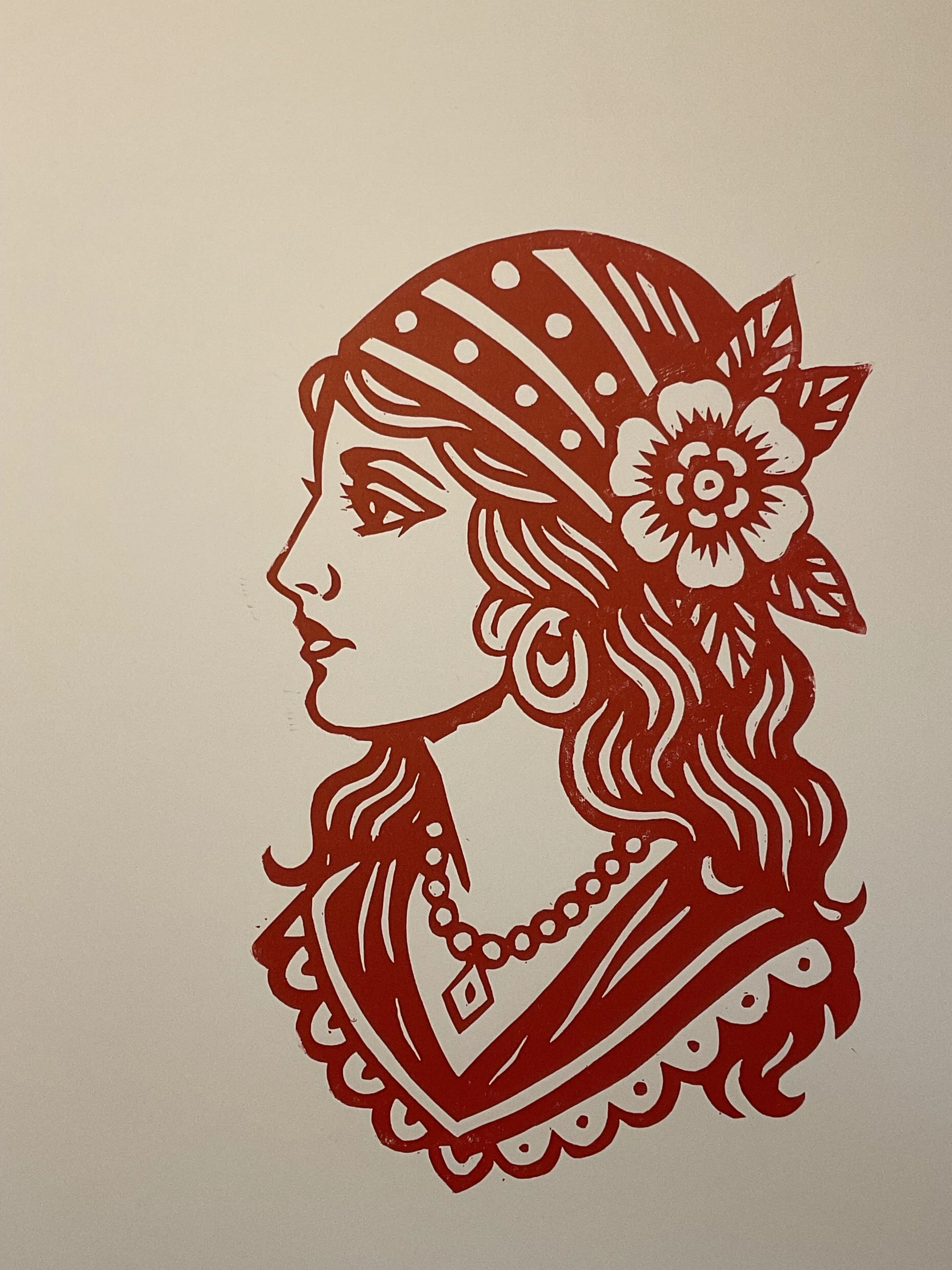 Red linocut print of a traditional tattoo-style gypsy woman with headscarf, flower and jewellery. Hand-carved and hand-printed by Elucidation Inc.”