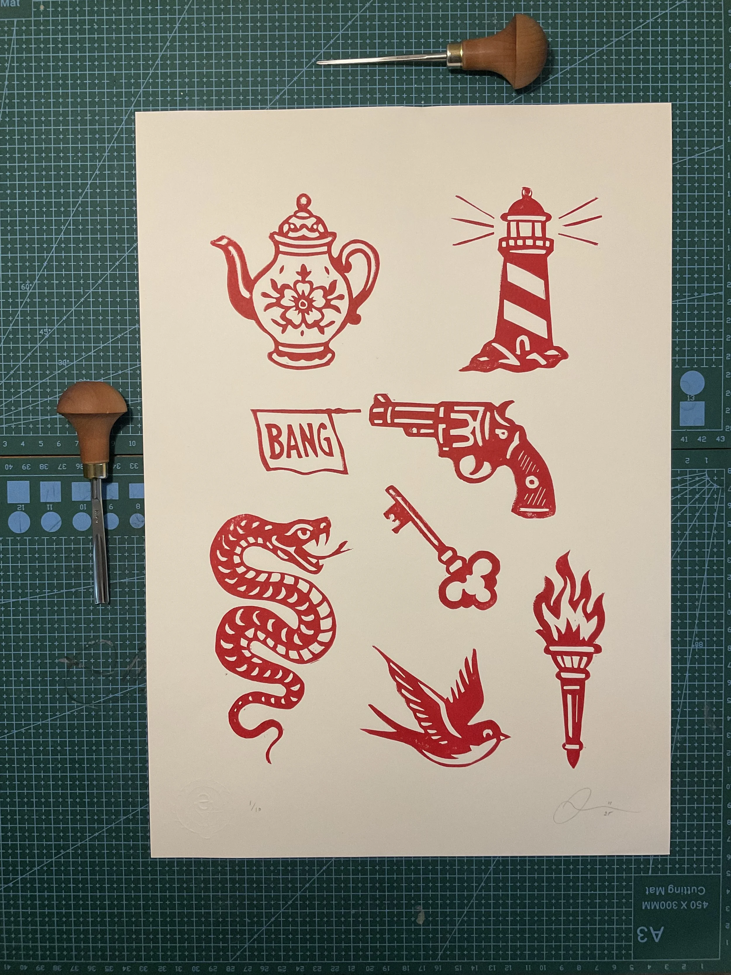 Red linocut tattoo flash print featuring a vintage teapot, lighthouse, revolver with ‘BANG’ flag, snake, key, swallow and flaming torch. Hand-carved and hand-printed by Elucidation Inc.