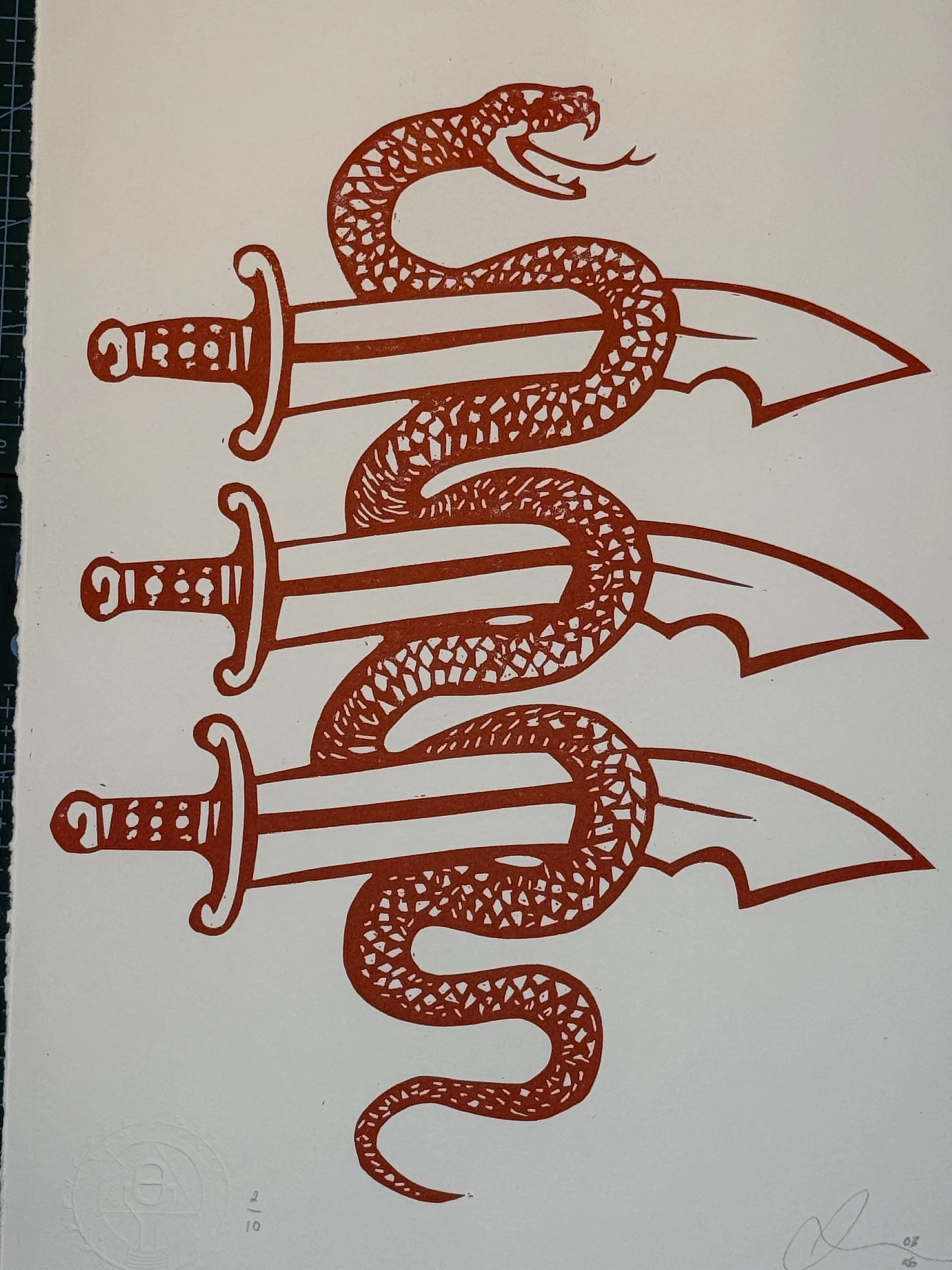 Hand printed linocut showing snake entwined with historic Essex three seaxes emblem