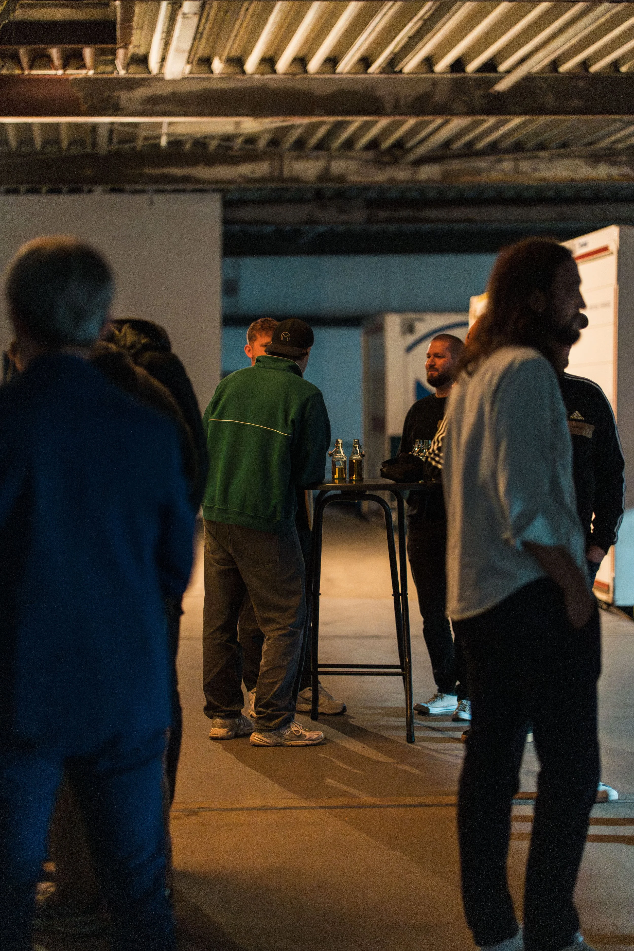 Gruppe von Leuten, die an einem Abend in einem Kellergang oder Lagerraum stehen, einige trinken Getränke, während sie sich unterhalten.