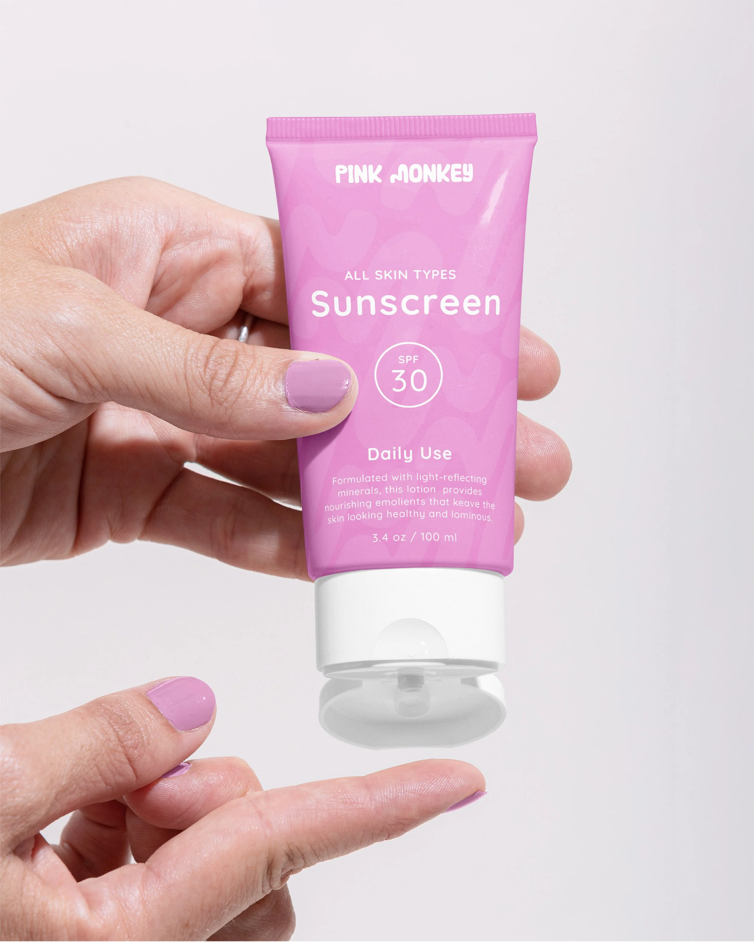 A hand holding a pink tube of Pink Monkey sunscreen with SPF 30, labeled for all skin types, on a white background.