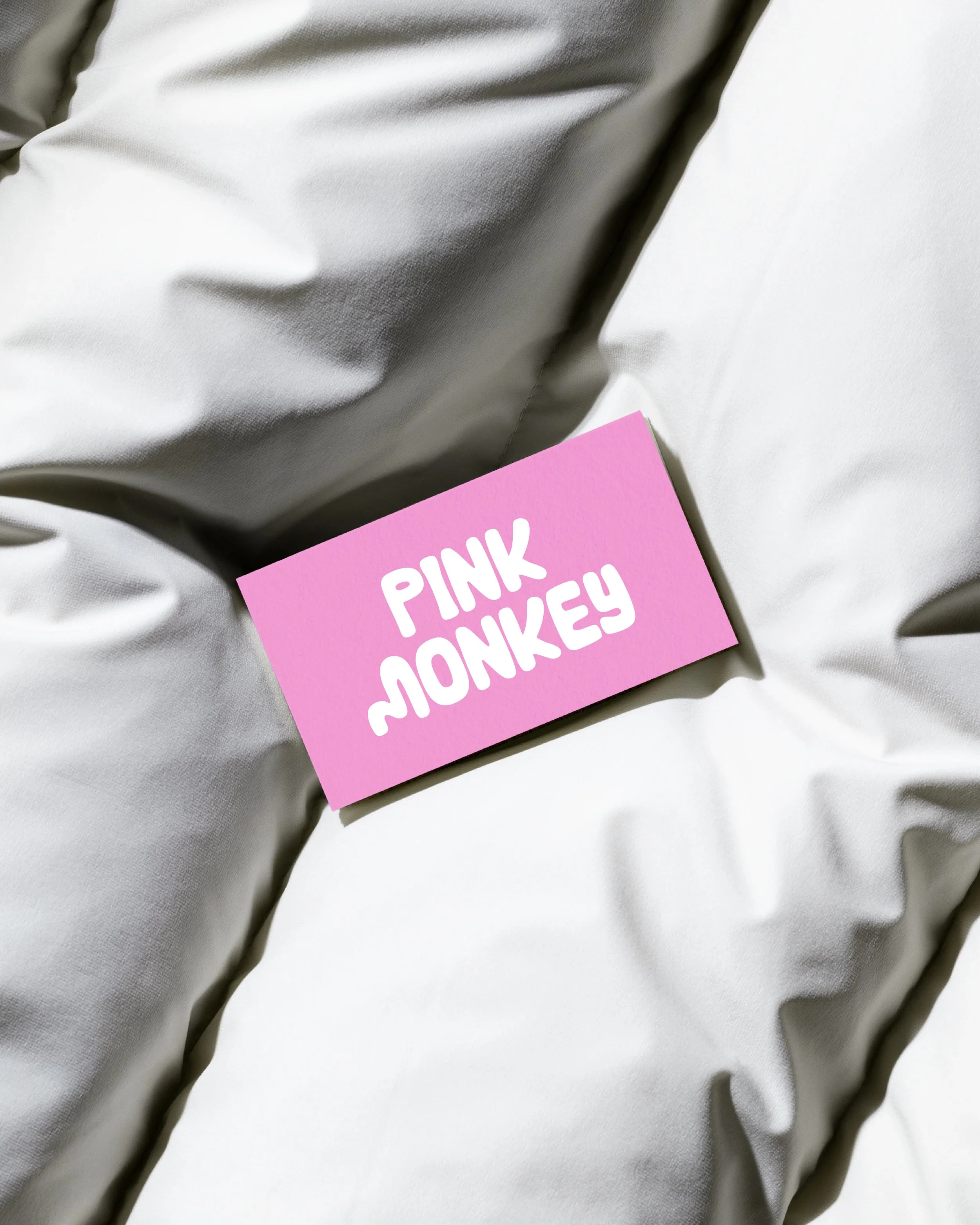 Pink card with white text that reads 'PINK MONKEY' resting on white fabric.