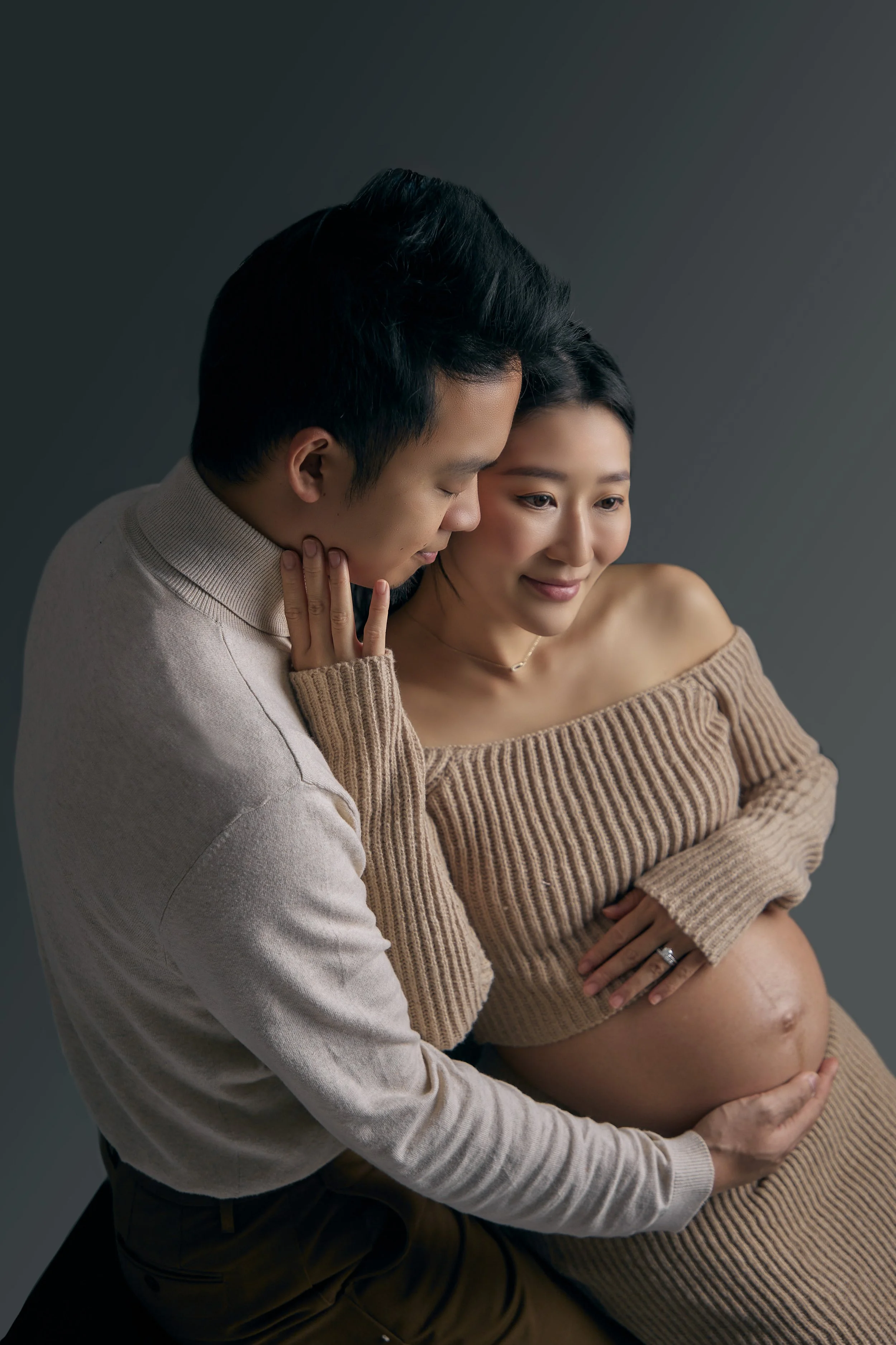 A pregnant woman and her partner sharing an intimate moment as he gently touches her belly, both smiling softly.