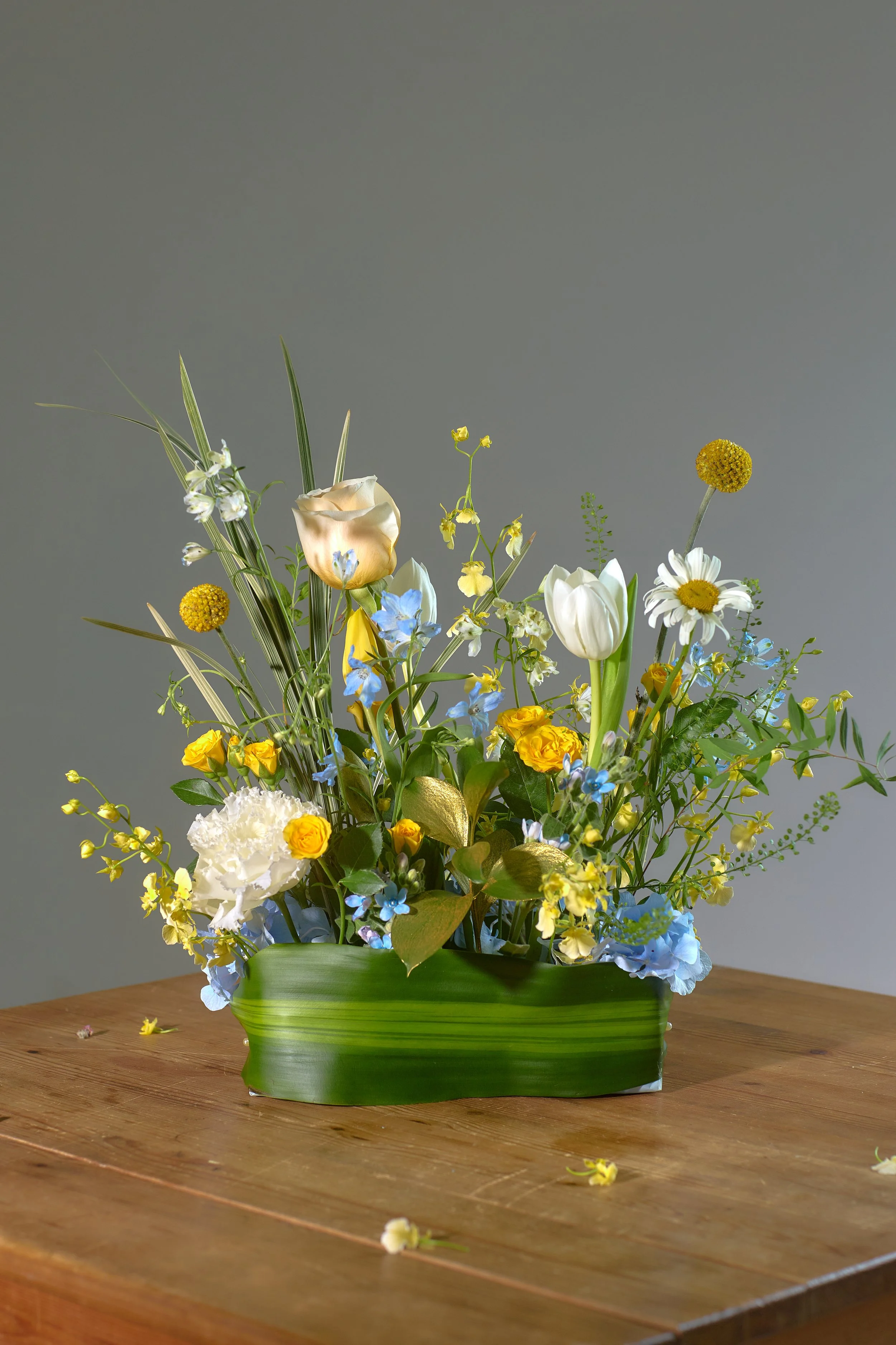 Arrangement of mixed flowers including tulips, daisies, and other blooms in a green container on a wooden table.