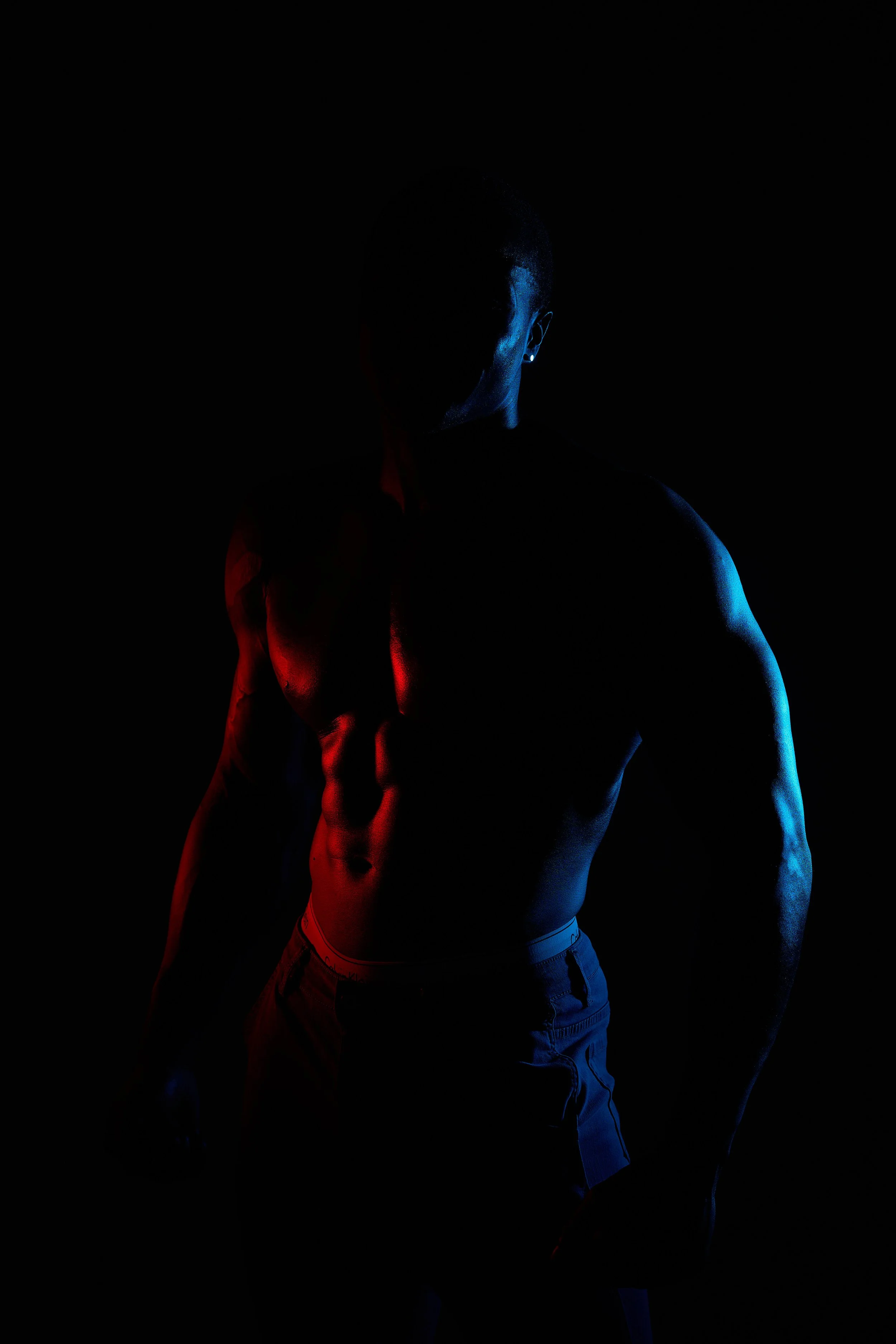 A silhouette of a muscular man with red and blue lighting highlighting his torso and arms against a dark background.
