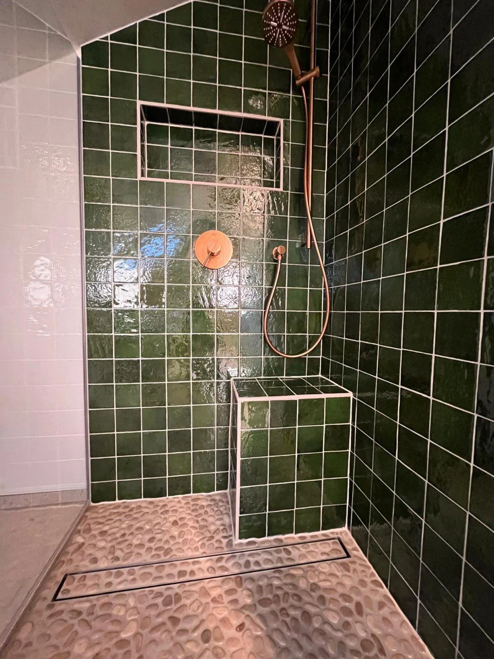 Moderne, bodengleiche Dusche mit hochwertiger Sanitärinstallation. Duschfläche ist mit dunkelgrünen, glänzenden Keramikfliesen im Quadratformat ausgestattet und verfügt über eine integrierte Wandnische sowie eine gemauerte Sitzbank. Der rutschfeste K
