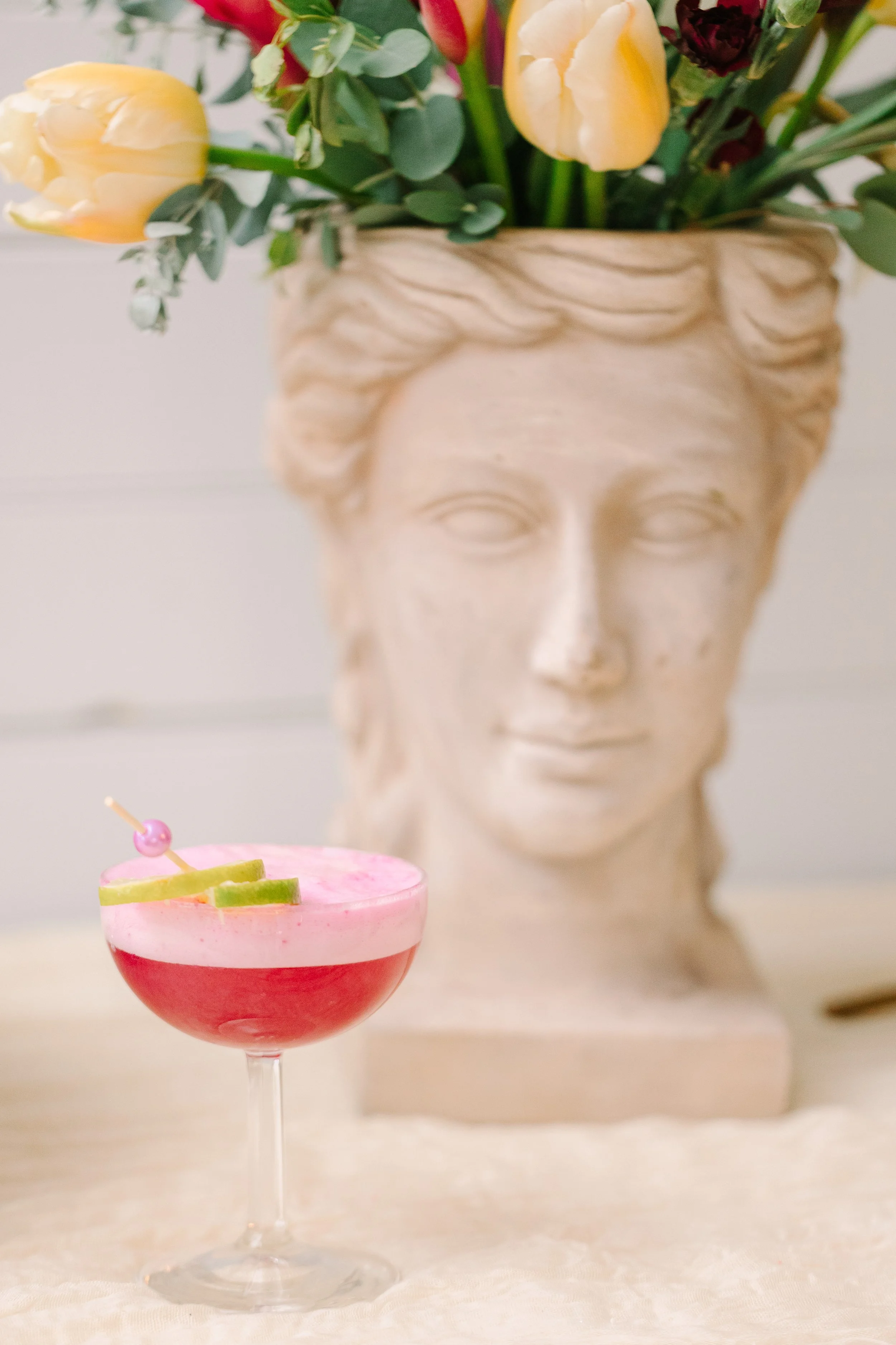 Vibrant tropical cocktail with lime slices, in front of a floral sculpture vase.