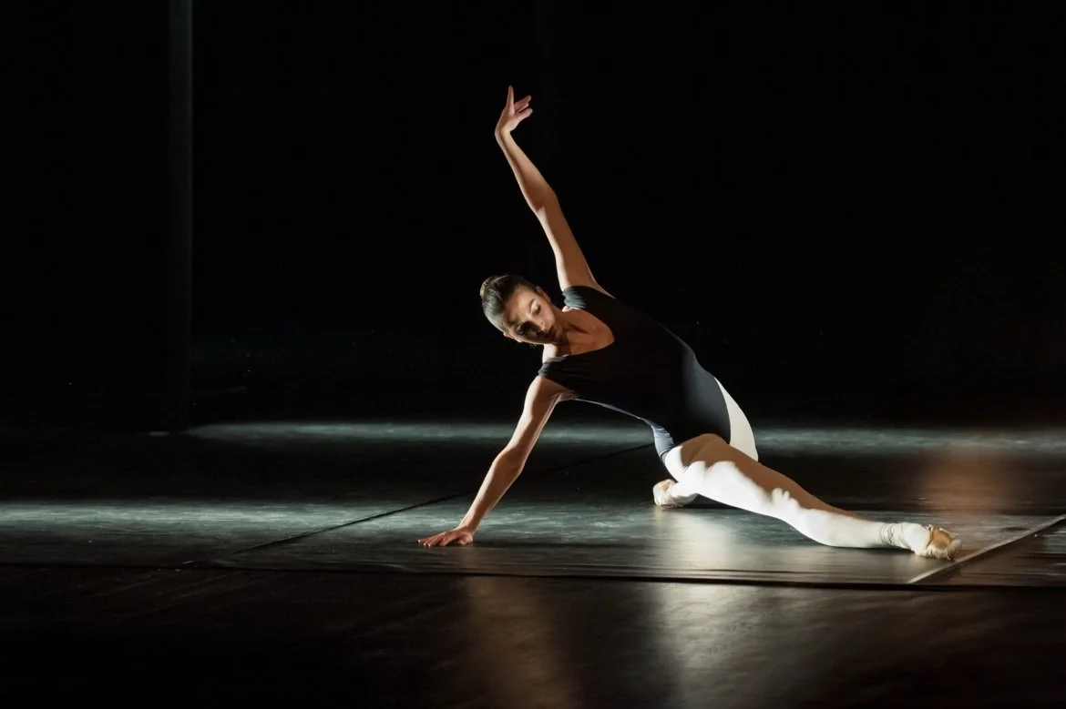 Femme danseuse en costume noir et blanc effectuant une pose sur scène sombre.
