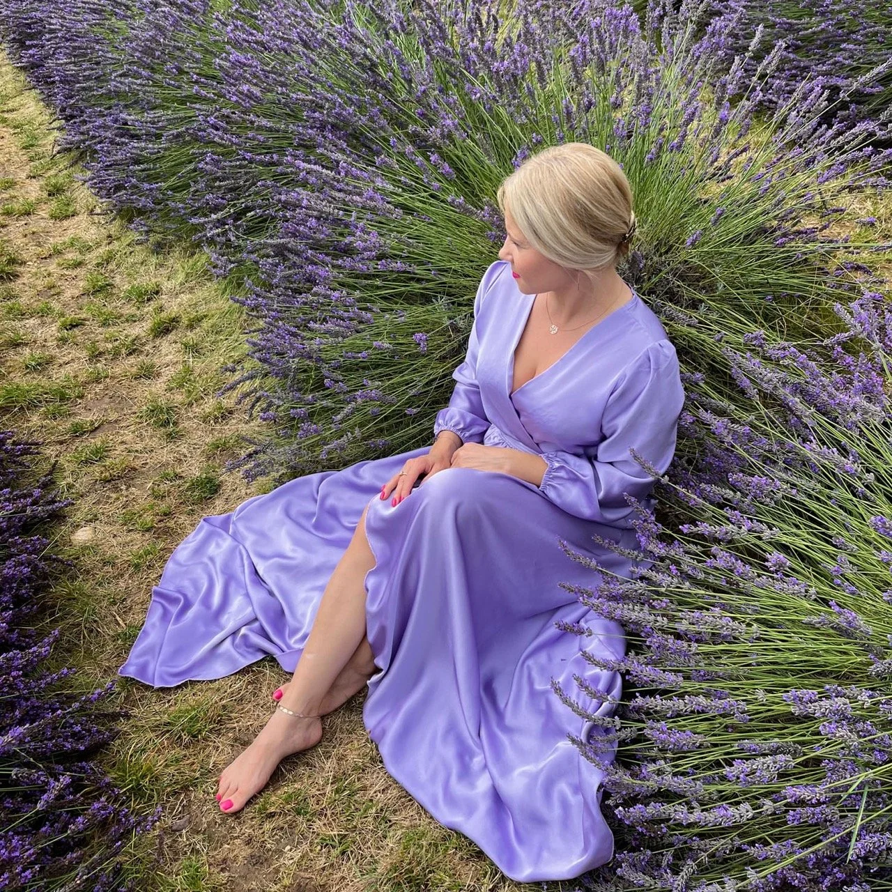 Oksana Pal, Psychologische Beraterin und Transformationscoach, sitzt in einem Fliederfeld und blickt nachdenklich in die Ferne – ein Bild, das ihre ruhige, einfühlsame Haltung und die Unterstützung symbolisiert, die sie ihren Klienten bietet.