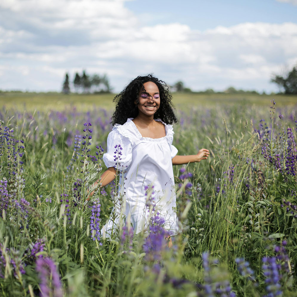Eine Frau tanzt im Fliederfeld, mit geschlossenen Augen und einem Lächeln auf den Lippen – ein Ausdruck von Freiheit, Freude und dem Leben in Selbstbestimmung.