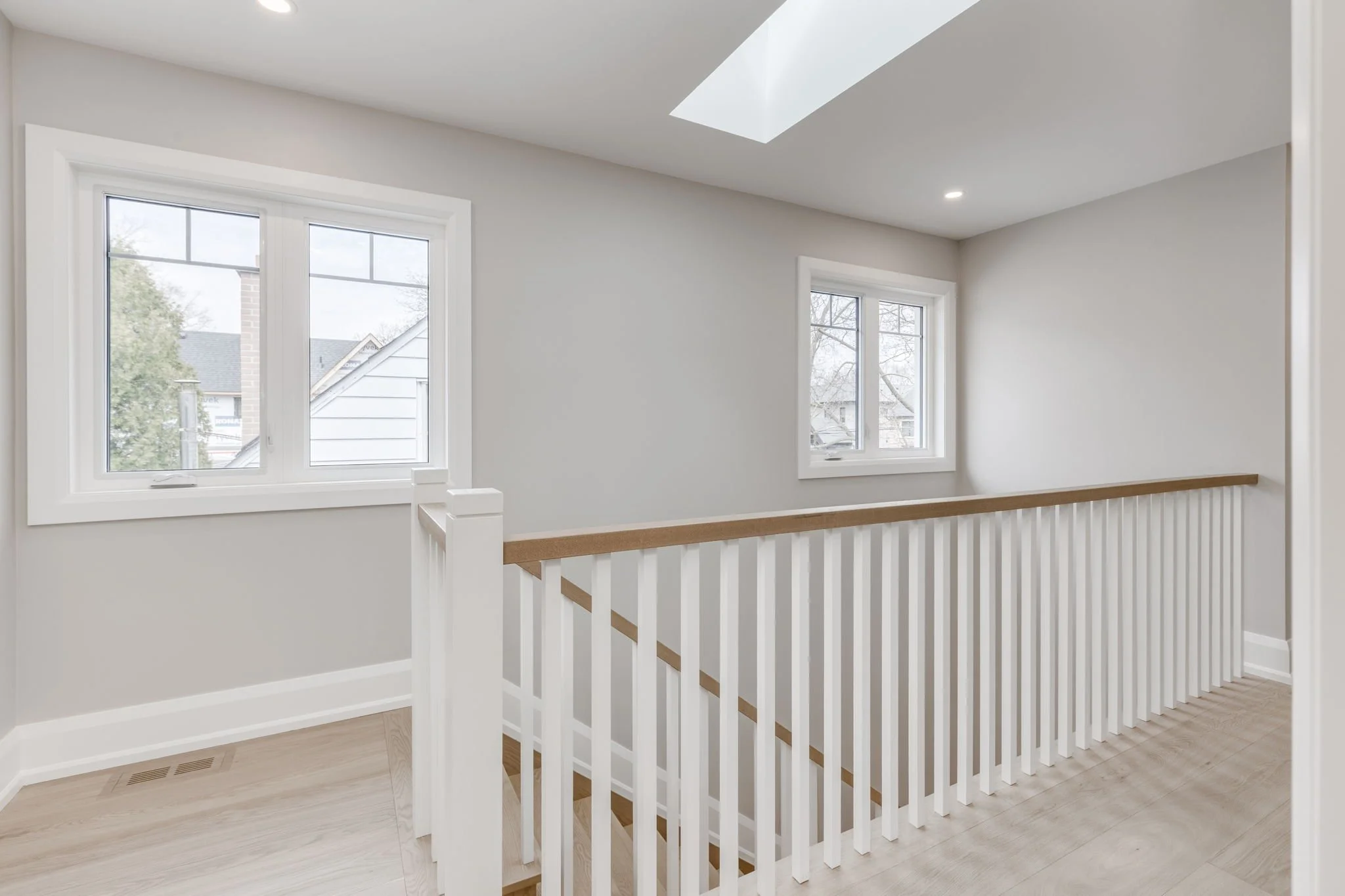 After renovation by Waterfront, an upper landing with skylight, white balustrade, and natural wood handrail in Etobicoke.