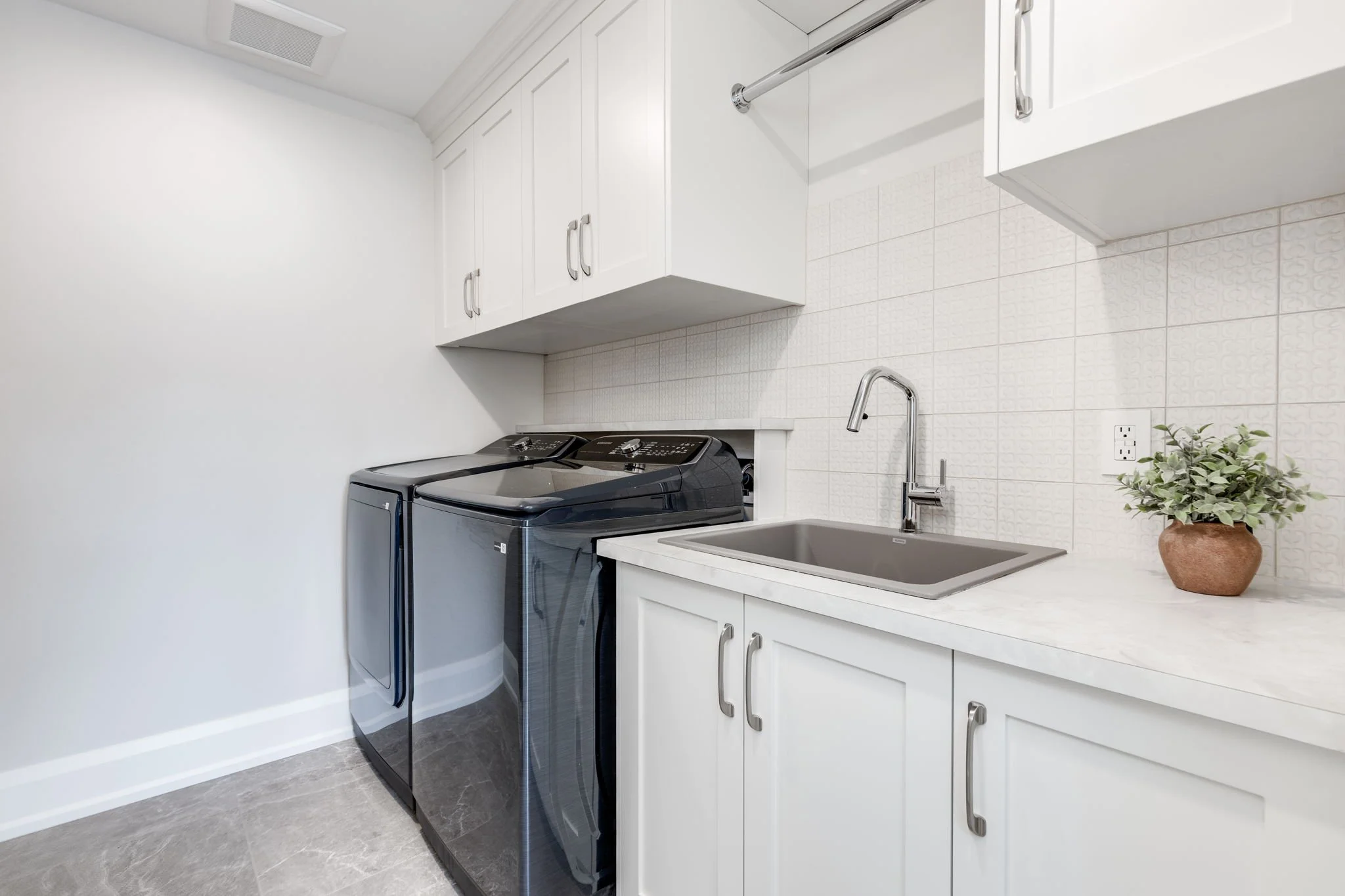 Basement apartment laundry room with washer and dryer appliances and a stainless steel with custom cabinetrysink, created by Waterfront Homes, a design-build firm in Toronto