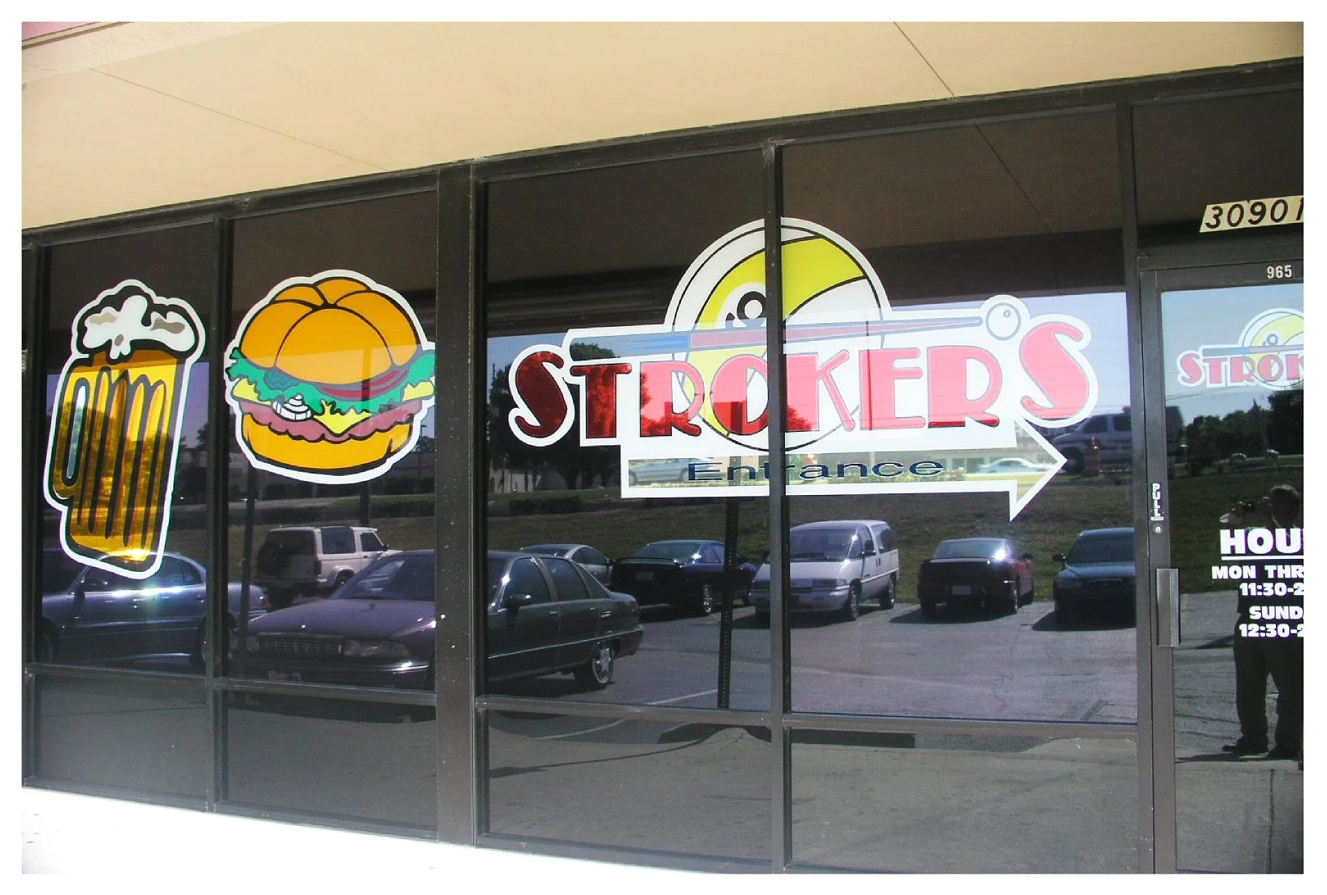 Glass storefront with decals of a frothy beer mug, a sandwich, and the text 'STROKER'S.' Visible parking lot reflection.