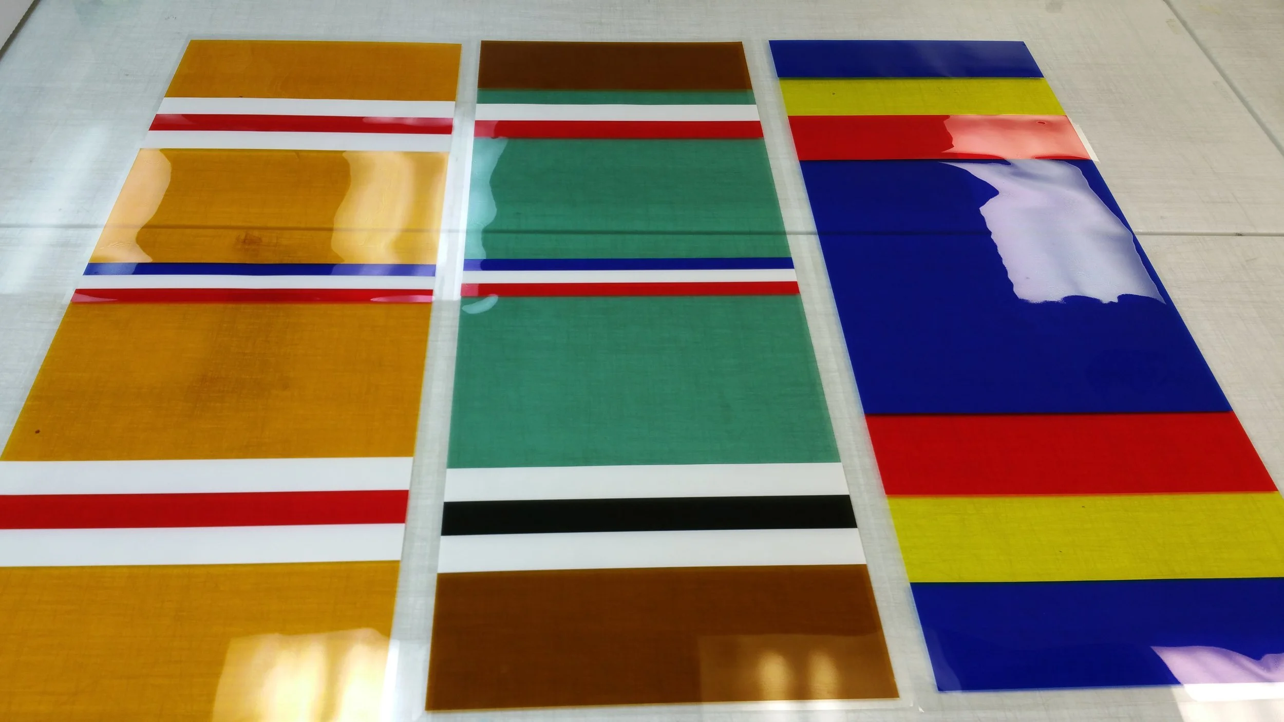 Color window tint.  Three sheets of colorful acrylic or plastic material with flag designs, laid flat on a white surface.