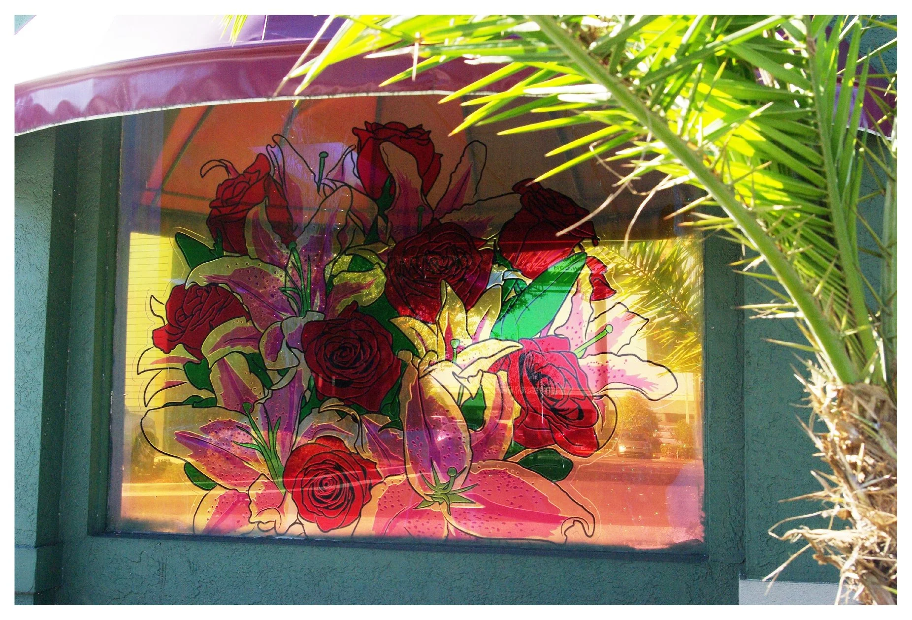 Stained glass window with floral design featuring roses and lilies, surrounded by palm leaves. colored window film