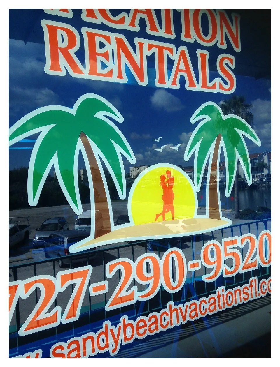 Vacation rental advertisement with palm trees and sunset graphic on a window. colored window film