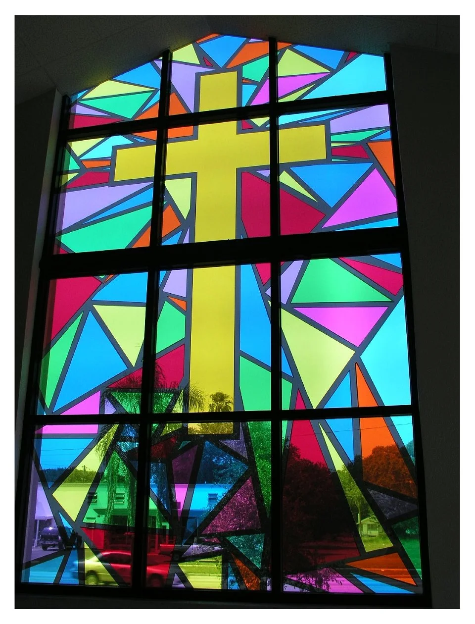Stained glass window featuring a large yellow cross with colorful geometric patterns. colored window film