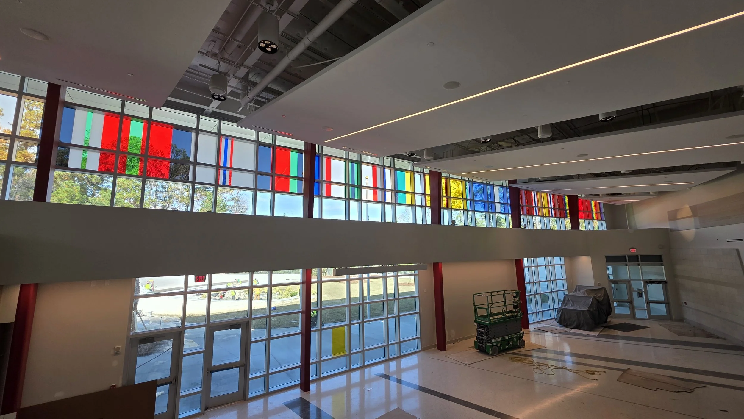 Interior of a building with large colored window film, construction equipment, and some covered objects.