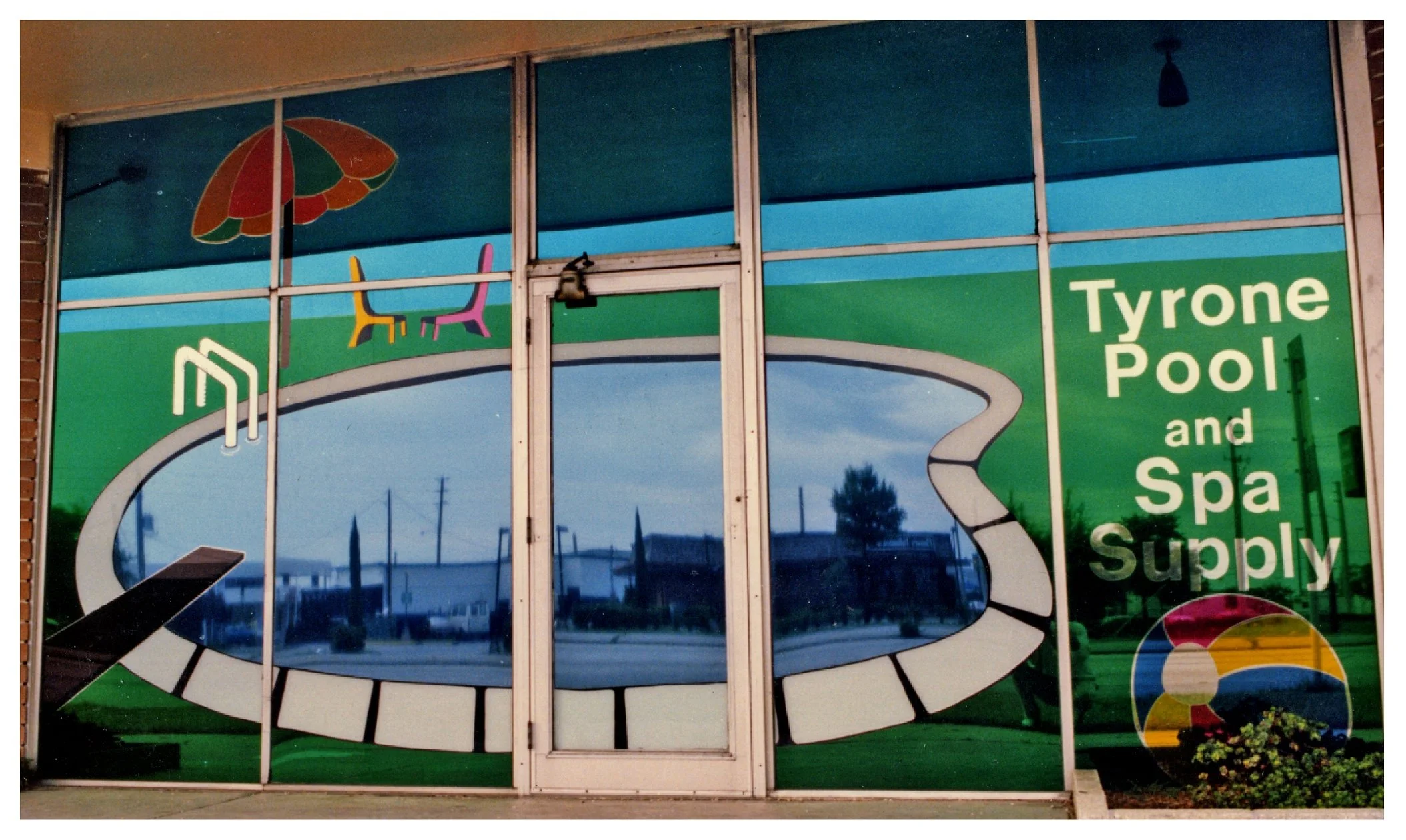 Storefront display with Tyrone Pool and Spa Supply logo, featuring a graphic of a swimming pool and beach elements on the window. colored window film