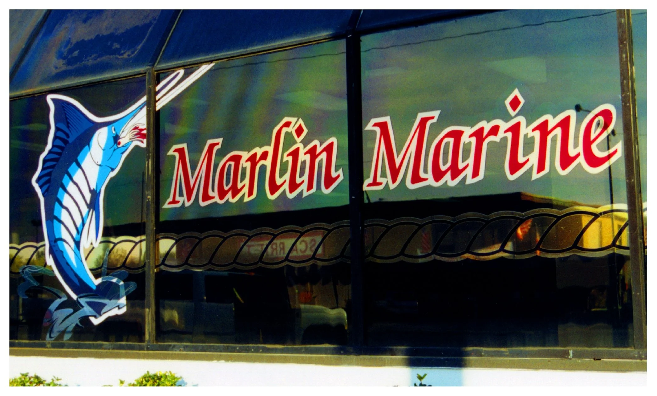Storefront window with 'Marlin Marine' text and a marlin graphic. colored window film