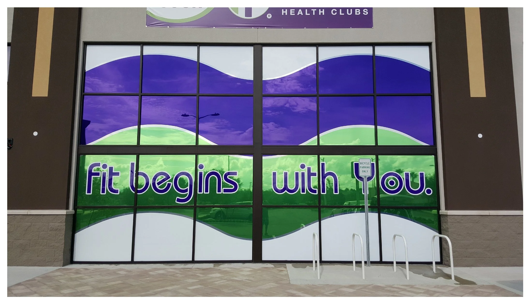 Fitness club window with slogan "fit begins with you" and bicycle parking. colored window film