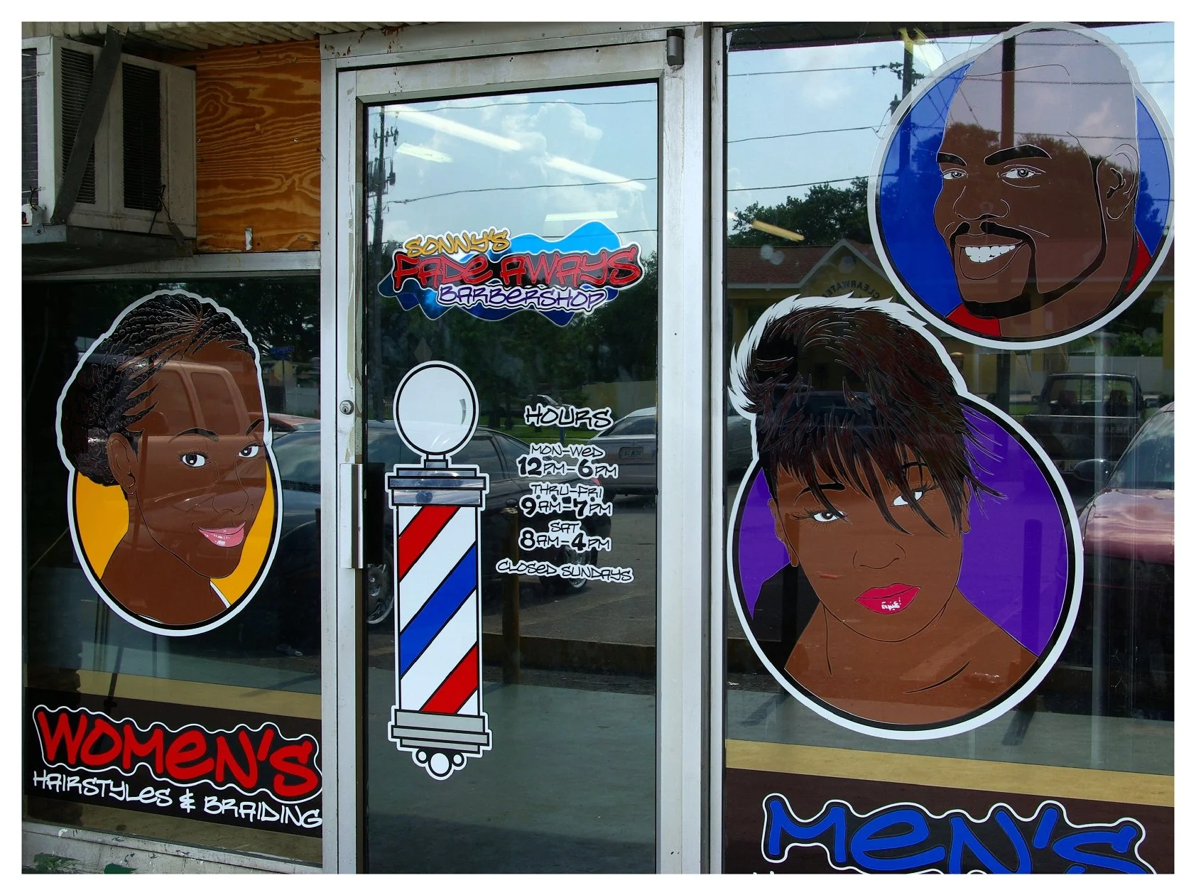 Barbershop storefront with cartoon faces advertising men's and women's hairstyling services. colored window film