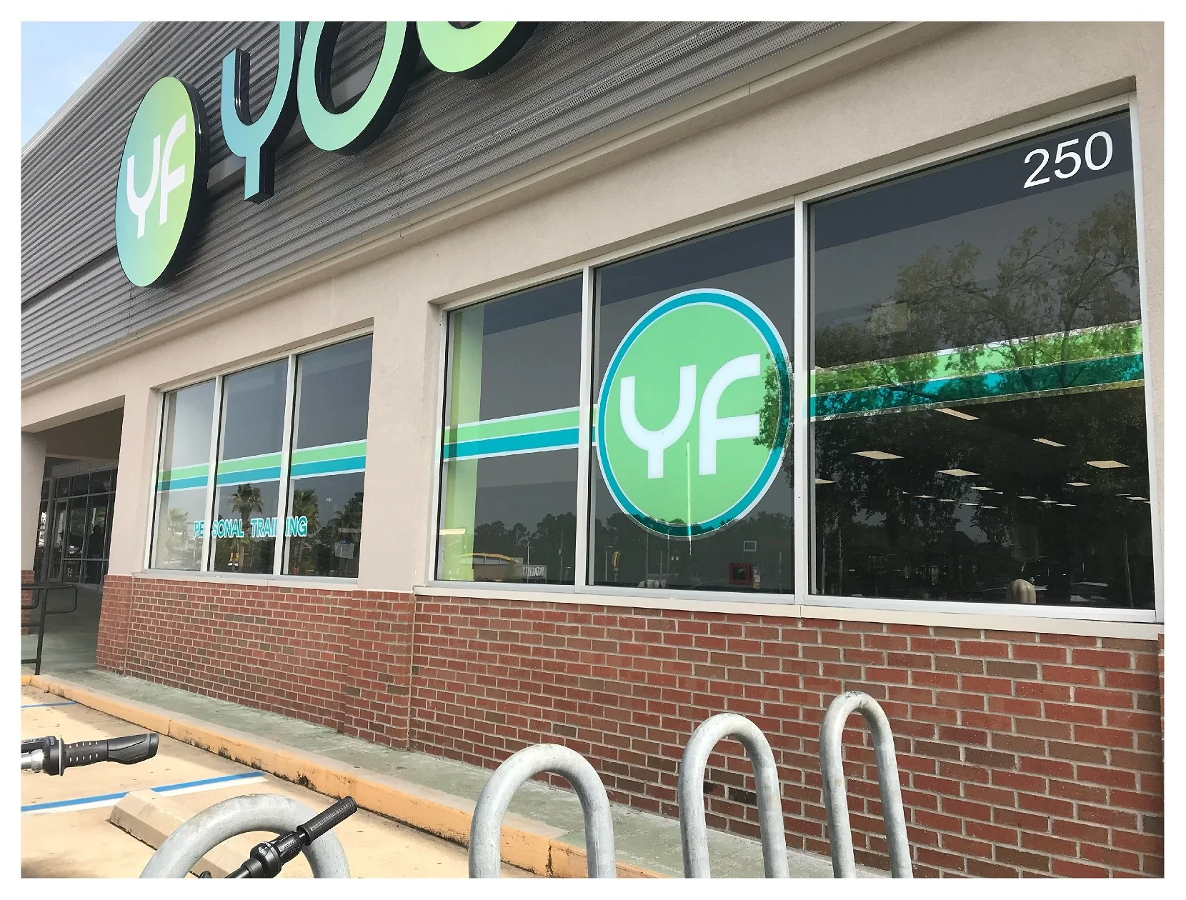 Exterior of a fitness center with a large "YF" logo and glass windows, located at number 250, featuring brick and concrete architecture. colored window film